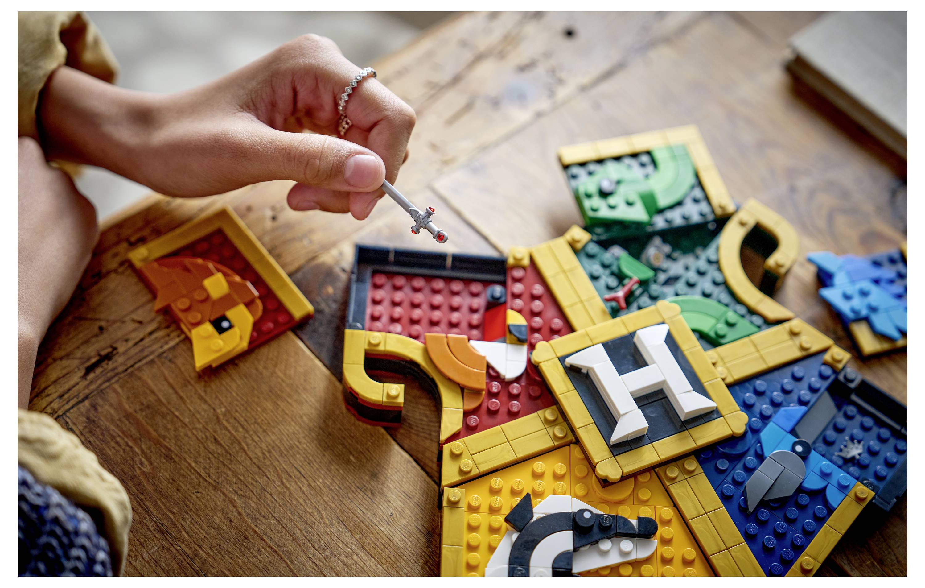 Ein Kind benutzt ein kleines Werkzeug, um ein buntes LEGO-ähnliches Puzzle auf einem Holztisch zusammenzubauen, wobei ineinandergreifende Teile eine große abstrakte Form bilden.