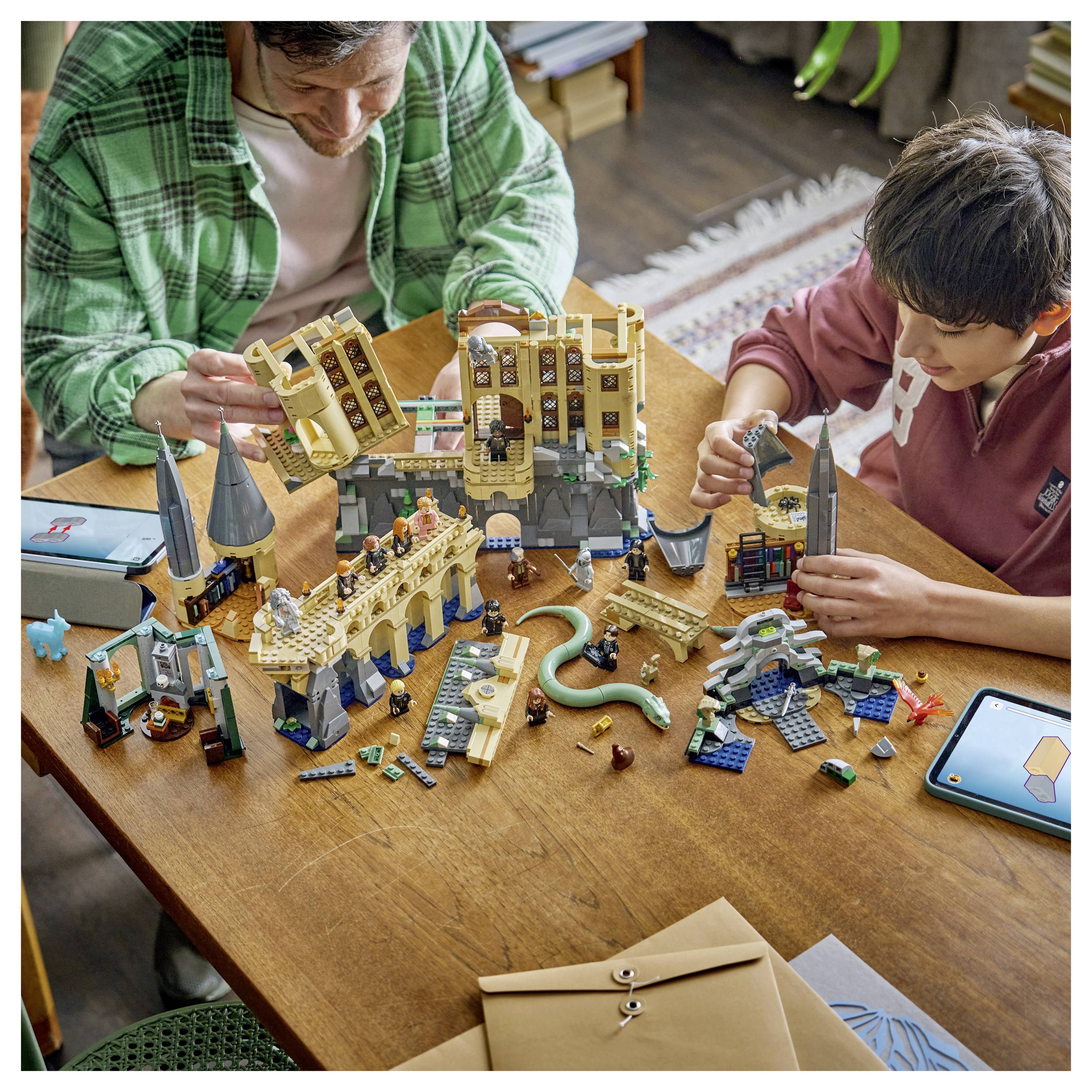 Ein Erwachsener und ein Kind bauen zusammen ein großes LEGO-ähnliches Burgensatz-Set an einem Holztisch mit verstreuten Teilen und Anleitung.