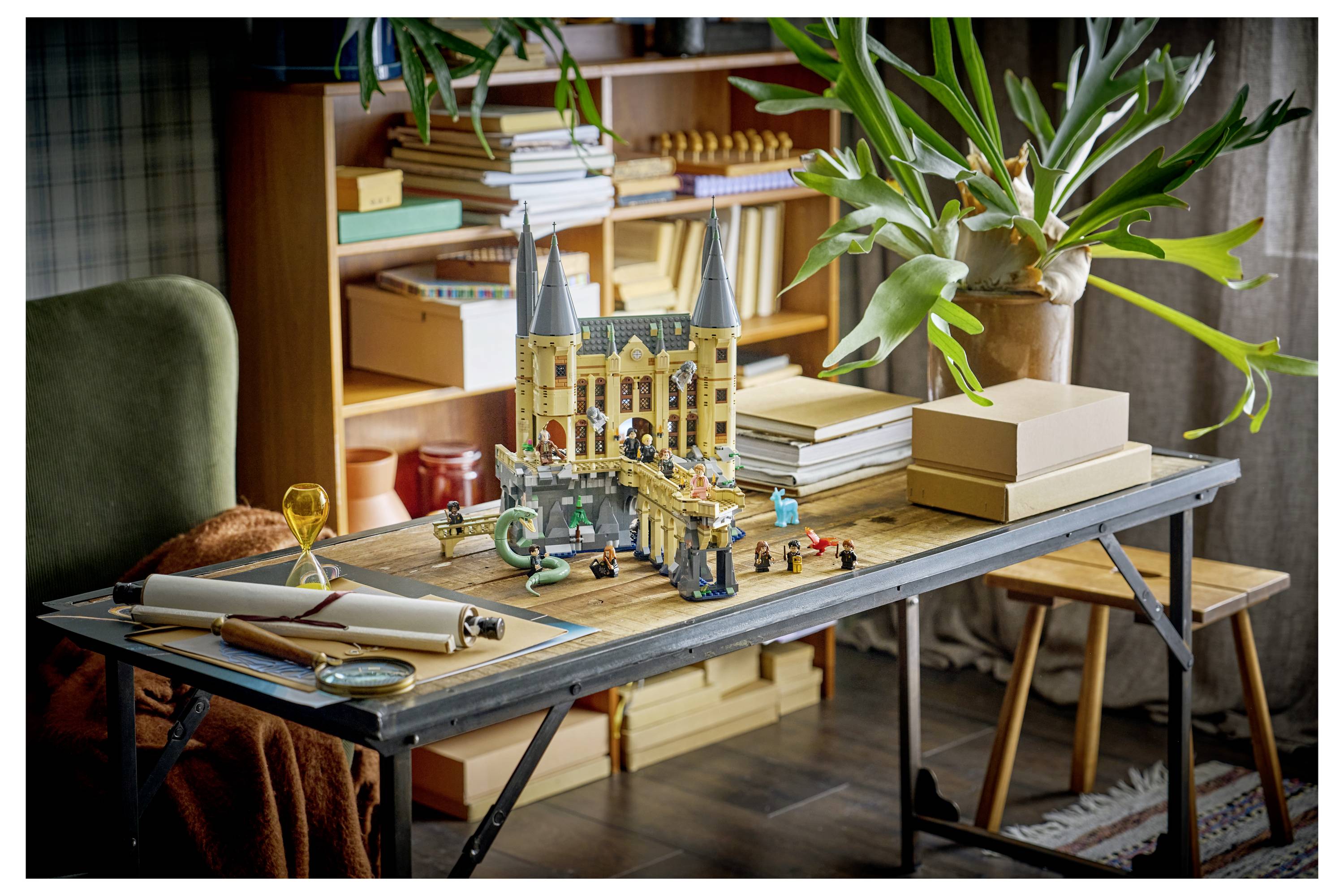 Ein Tischmodell einer gotischen Kathedrale im Bau, umgeben von Büchern, aufgerollten Plänen und einer Topfpflanze in einem gemütlichen Zimmer.