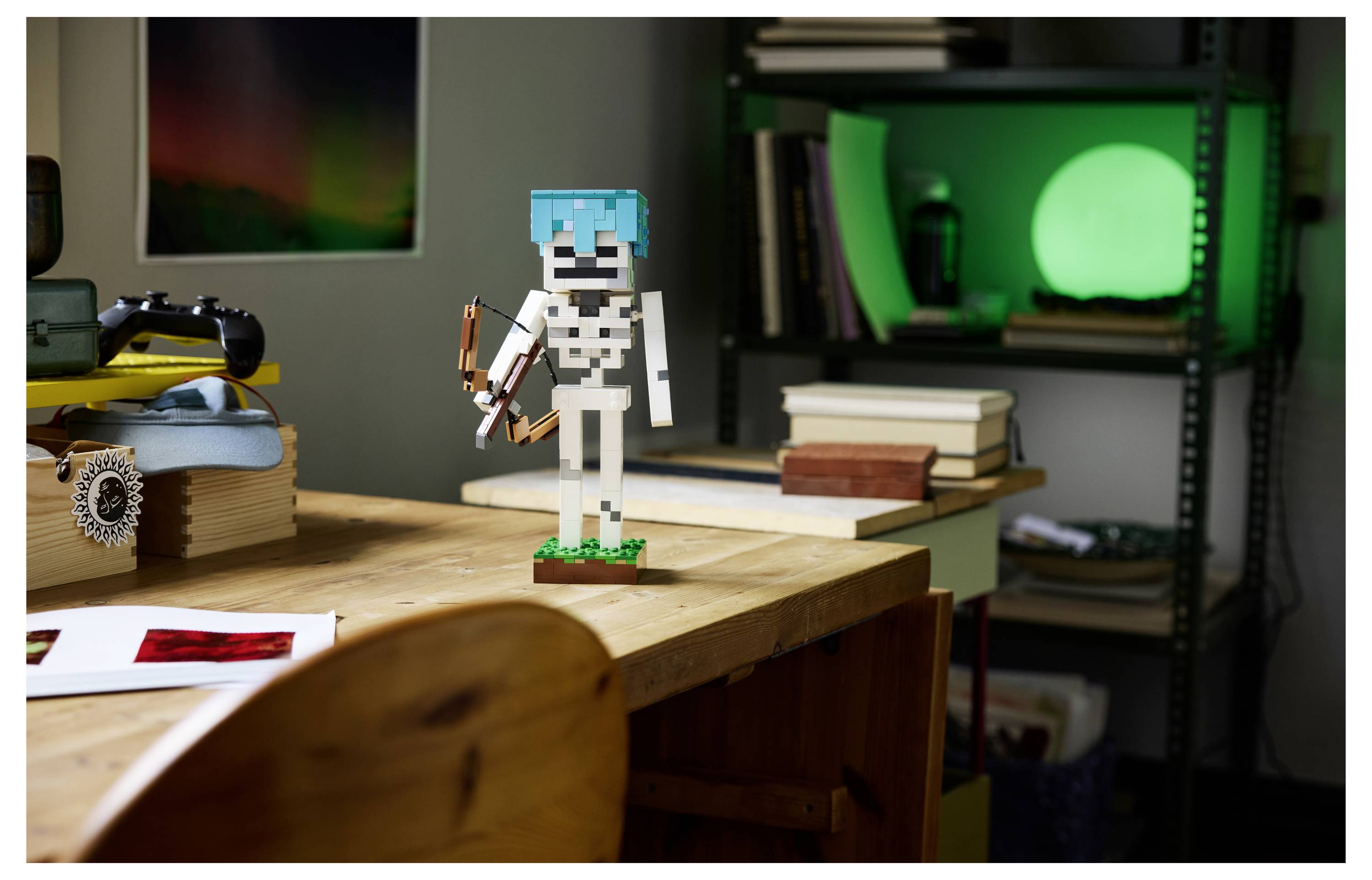 Eine kleine LEGO-ähnliche Skelettfigur mit einem blauen Helm steht auf einem Holzschreibtisch neben Büchern in einem Zimmer mit einer leuchtend grünen Lampe.