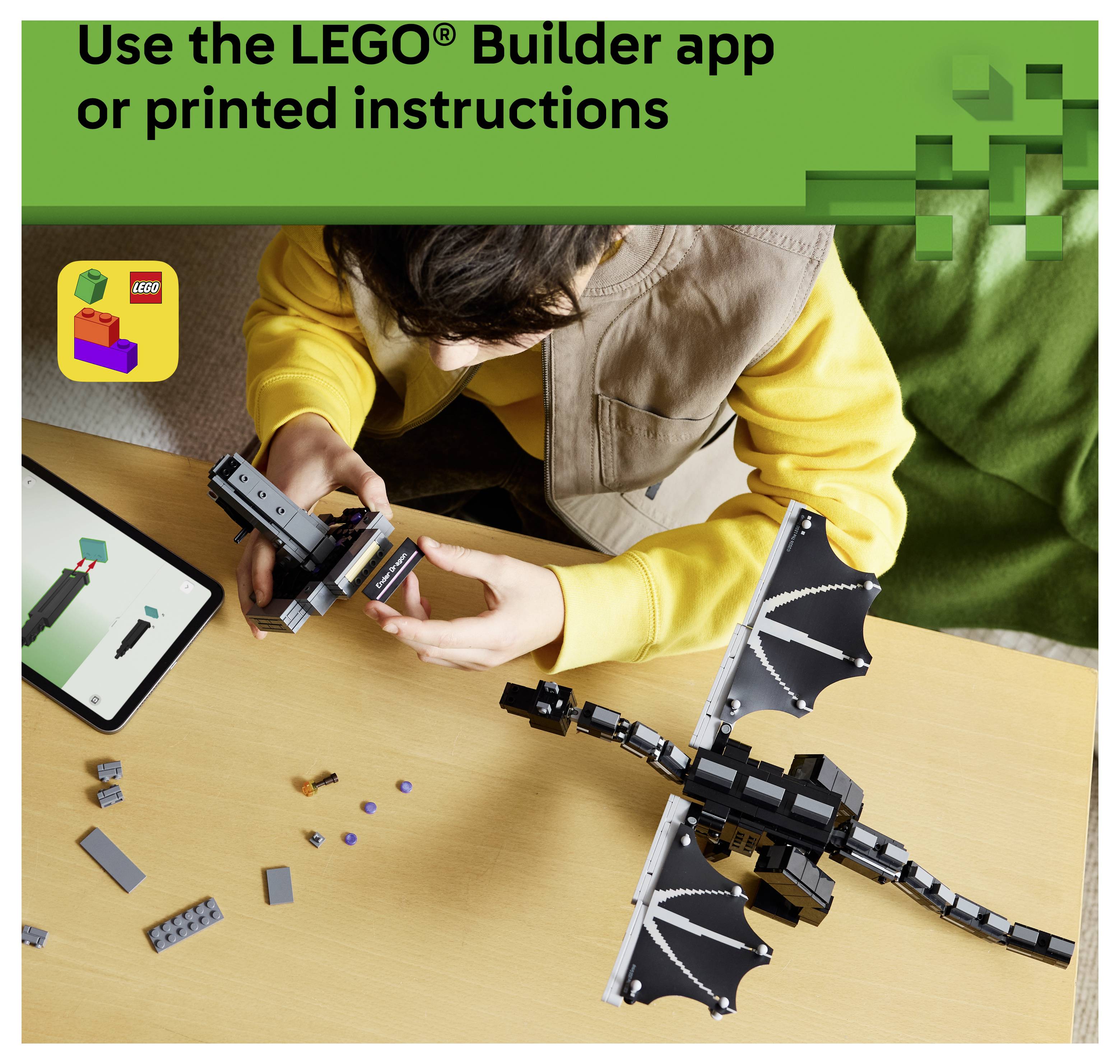 Person baut einen LEGO-Drachen mit der LEGO Builder App oder gedruckten Anleitung; Tablet zeigt Montagesschritte neben verstreuten Bausteinen.