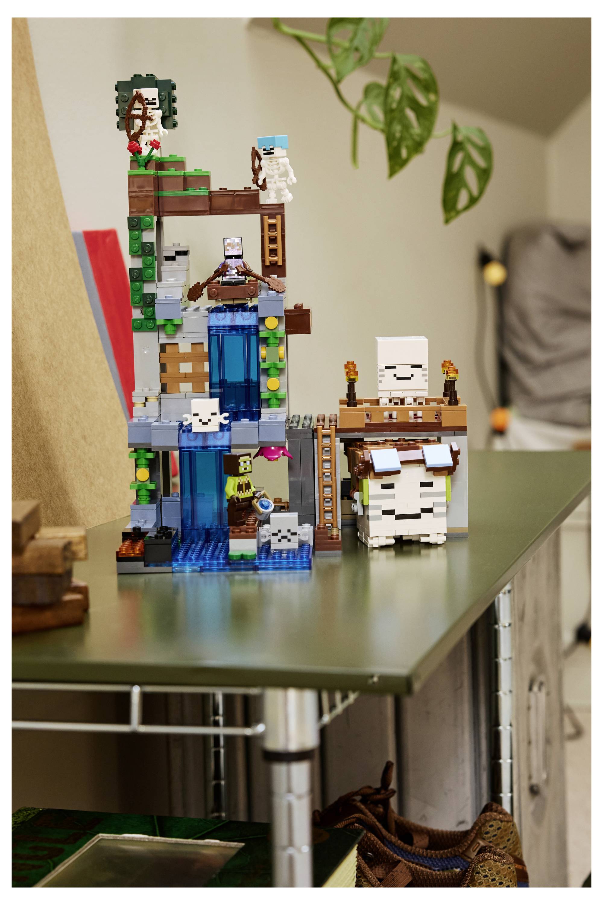 Ein LEGO Minecraft-Wehrturm mit Wasserfällen, Leitern und kleinen Blockfiguren sitzt auf einem Tisch in Innenräumen.