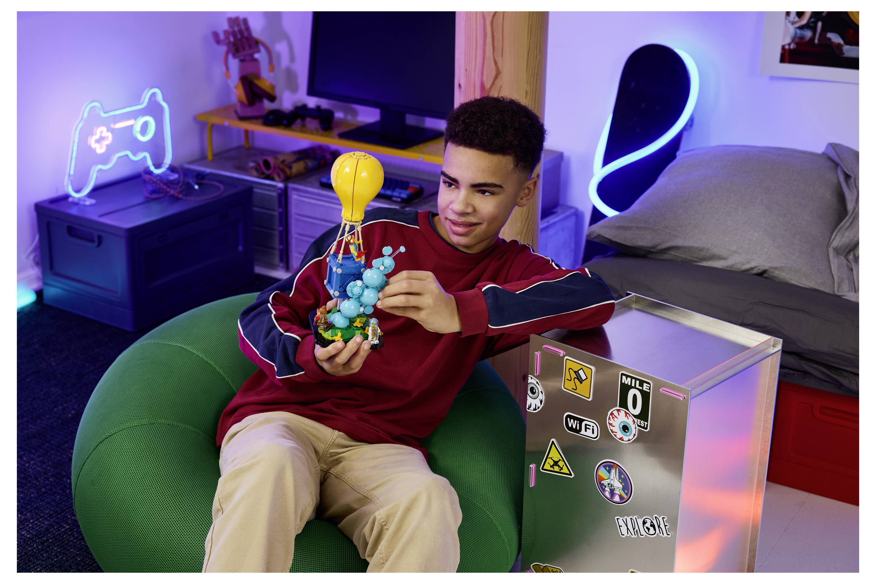 Teenagerboy, der sich in einem schlafzimmerähnlichen Gaming-Setup entspannt, montiert ein buntes Molekülmodell, während er in einem grünen Sitzsack sitzt.