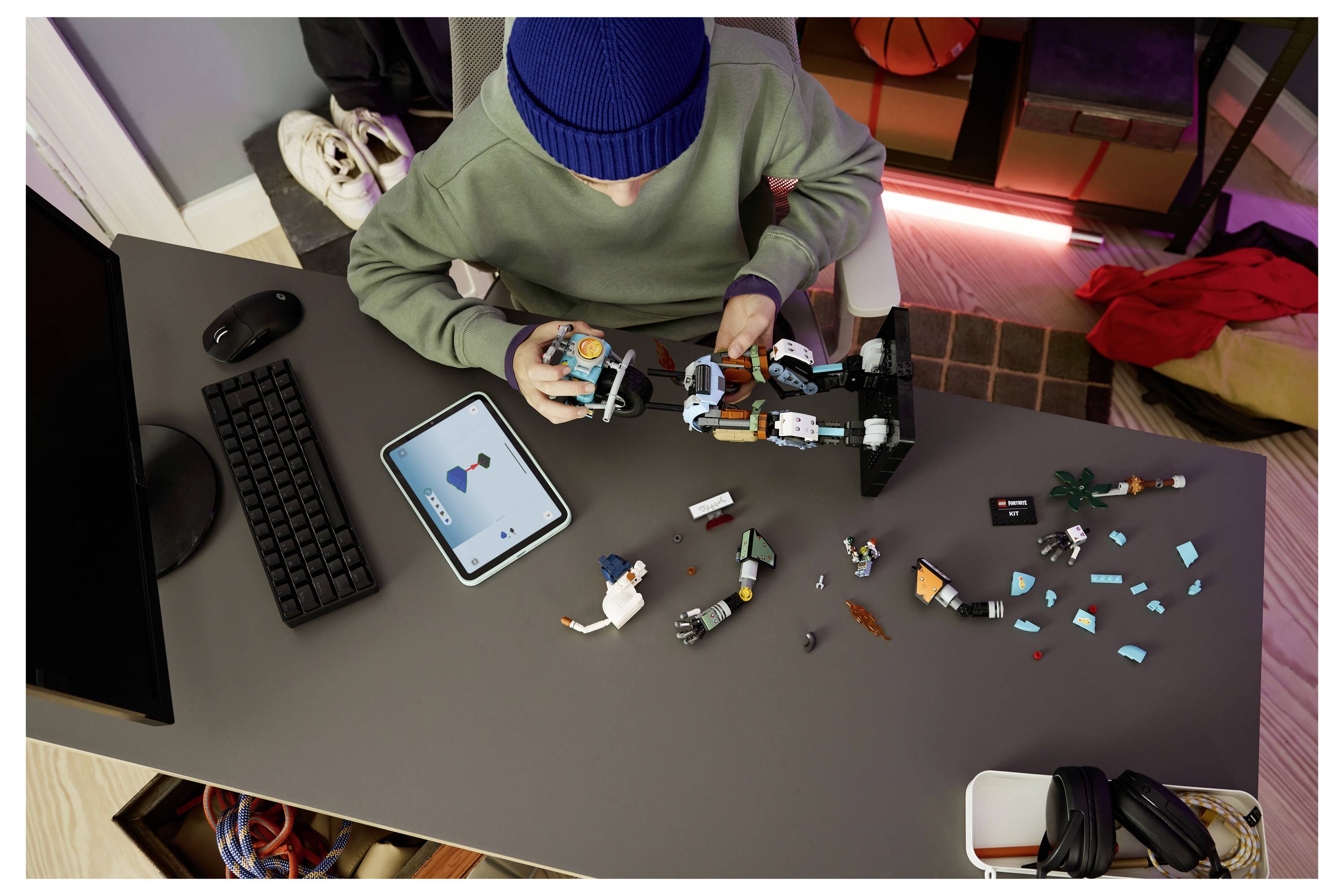 Eine Person baut einen LEGO-ähnlichen Roboter an einem Schreibtisch, während sie Anweisungen auf einem Tablet befolgt, mit verstreuten Teilen um sie herum.