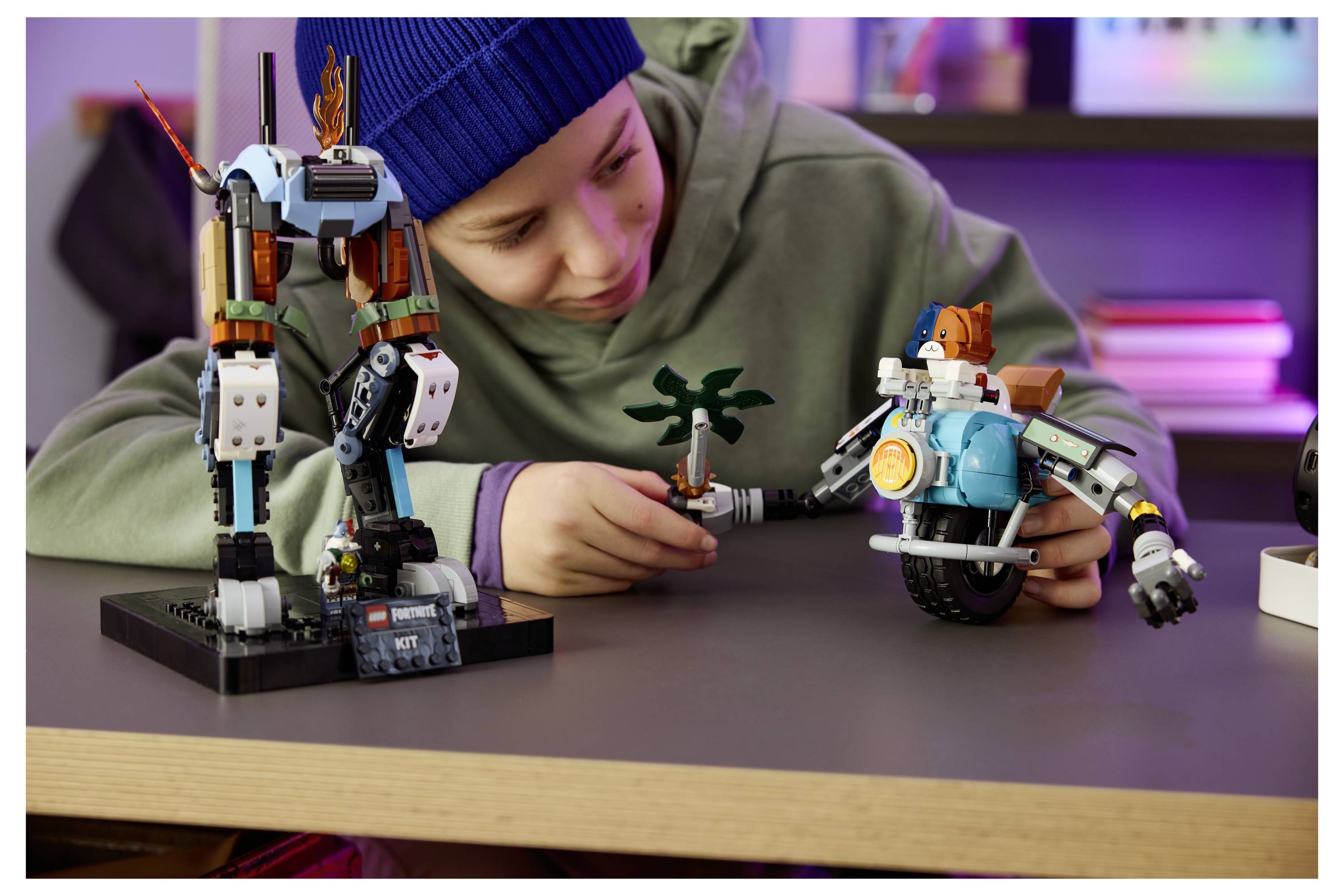 Kind in blauer Mütze spielt mit zwei Roboterspielzeugen und einer kleinen Palme auf einem Tisch und baut eine Science-Fiction-Szenerie.