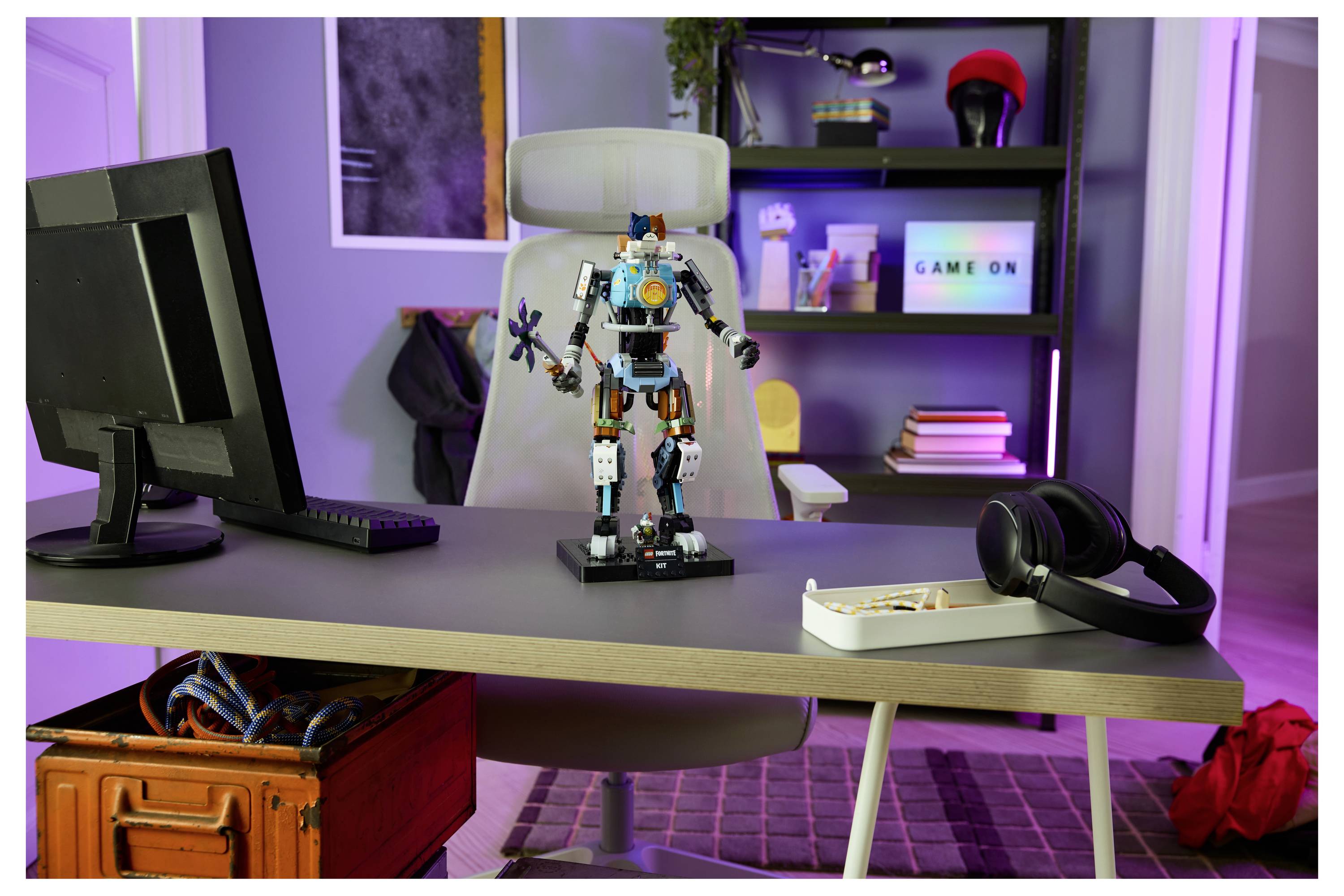 Schreibtischaufbau mit einer Roboterfigur in der Mitte des Tisches, Kopfhörern und Tastatur davor und einem „GAME ON