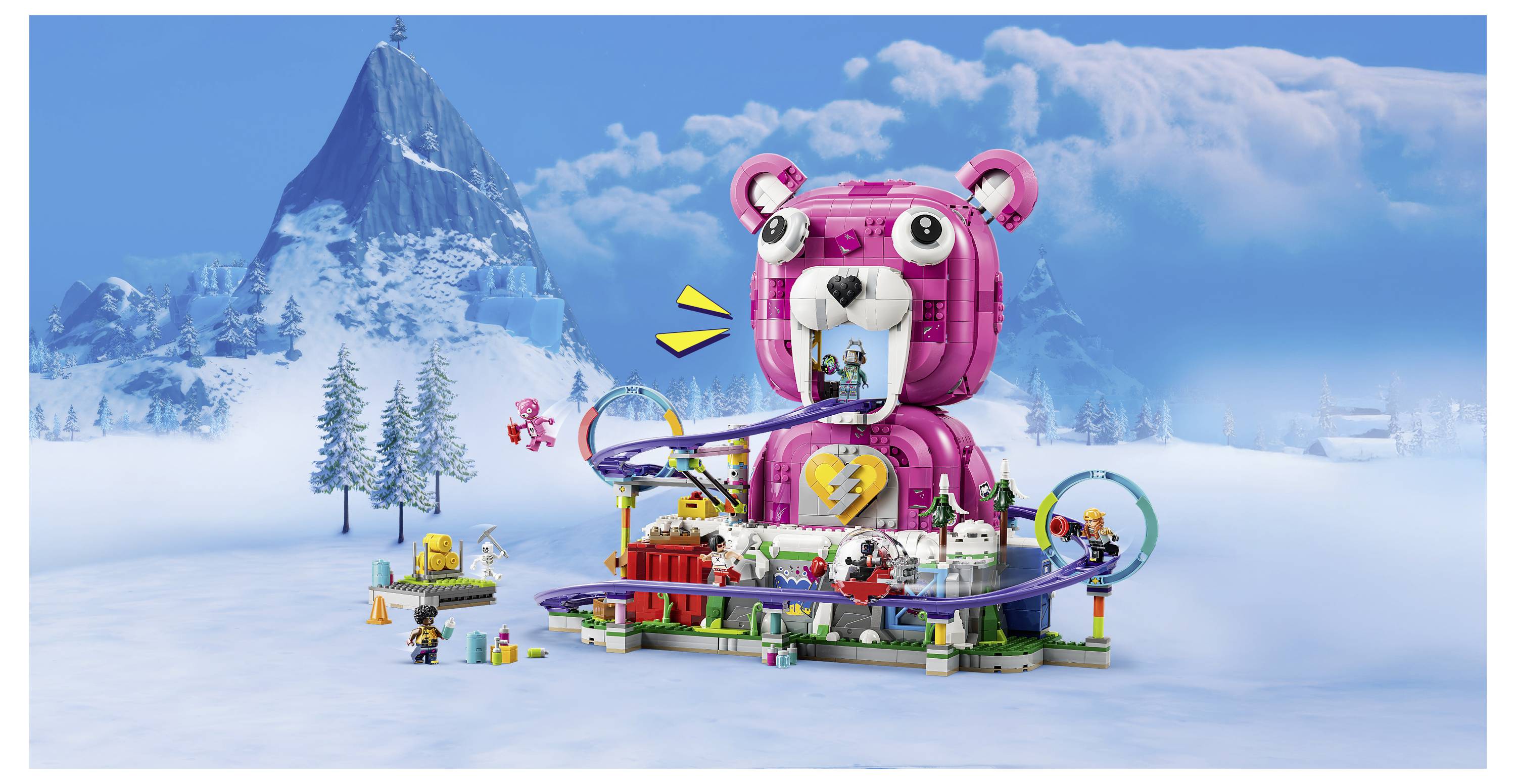 Buntes Spielzeugset mit einem riesigen rosa bärenförmigen Gebäude im Zentrum, Gleisen, Figuren und kleinen Fahrzeugen in einer verschneiten Berglandschaft.