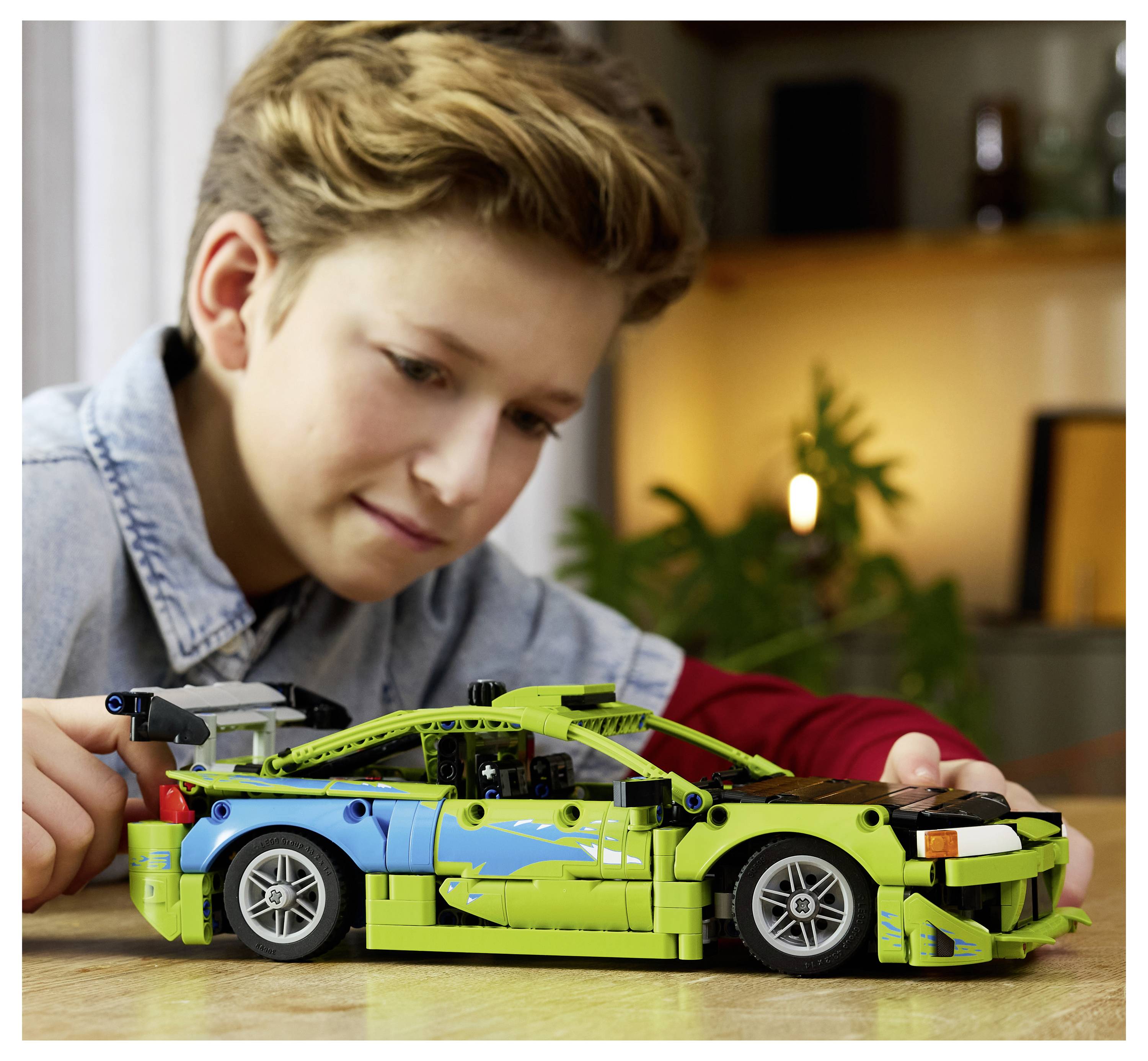 Ein Kind konzentriert sich, während es ein grünes und blaues Spielzeugauto-Modell auf einem Tisch zusammenbaut.