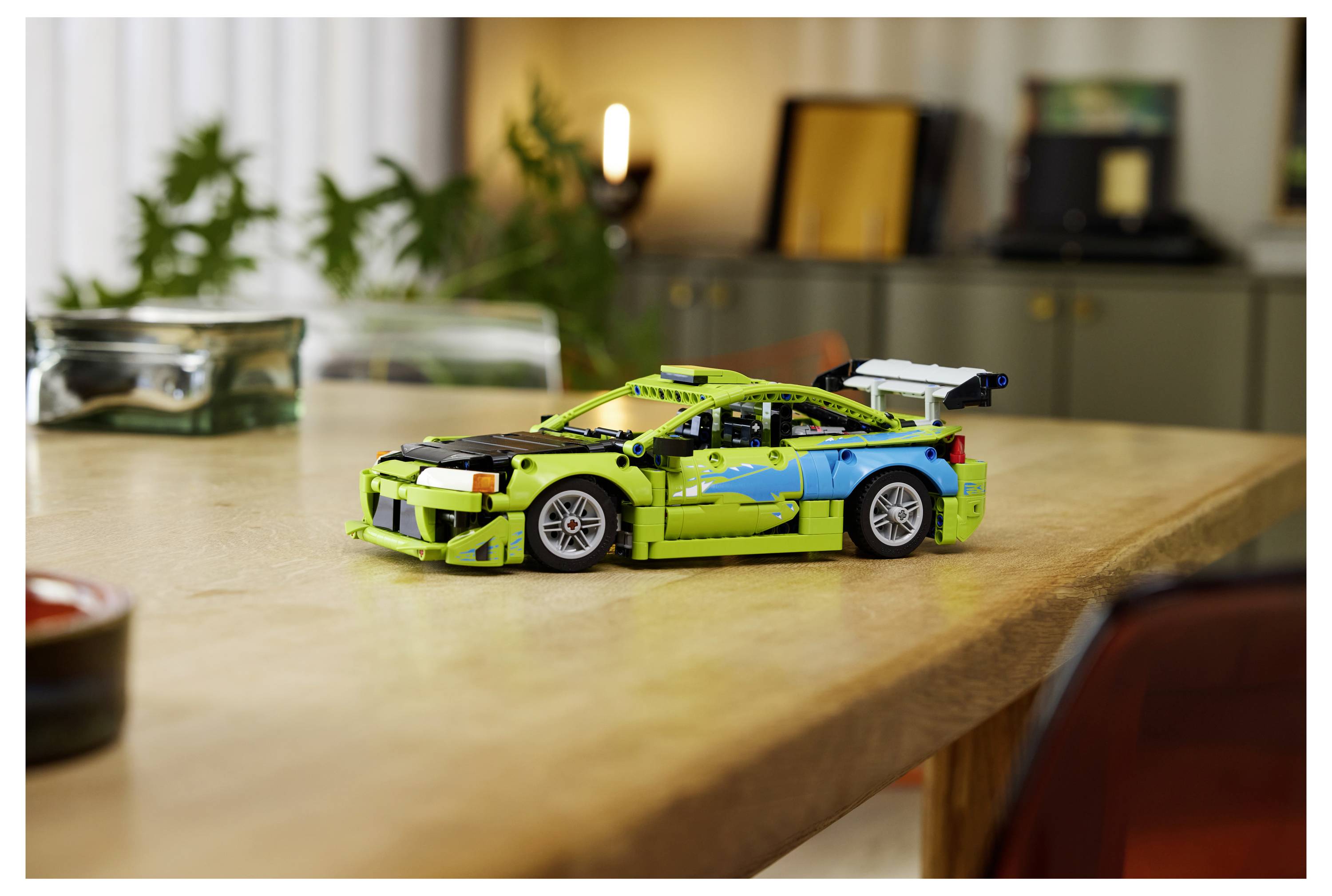 Ein limonen-grünes und blaues LEGO-Rennwagen-Modell sitzt auf einem Holztisch in einem sanft unscharfen Innenraum.
