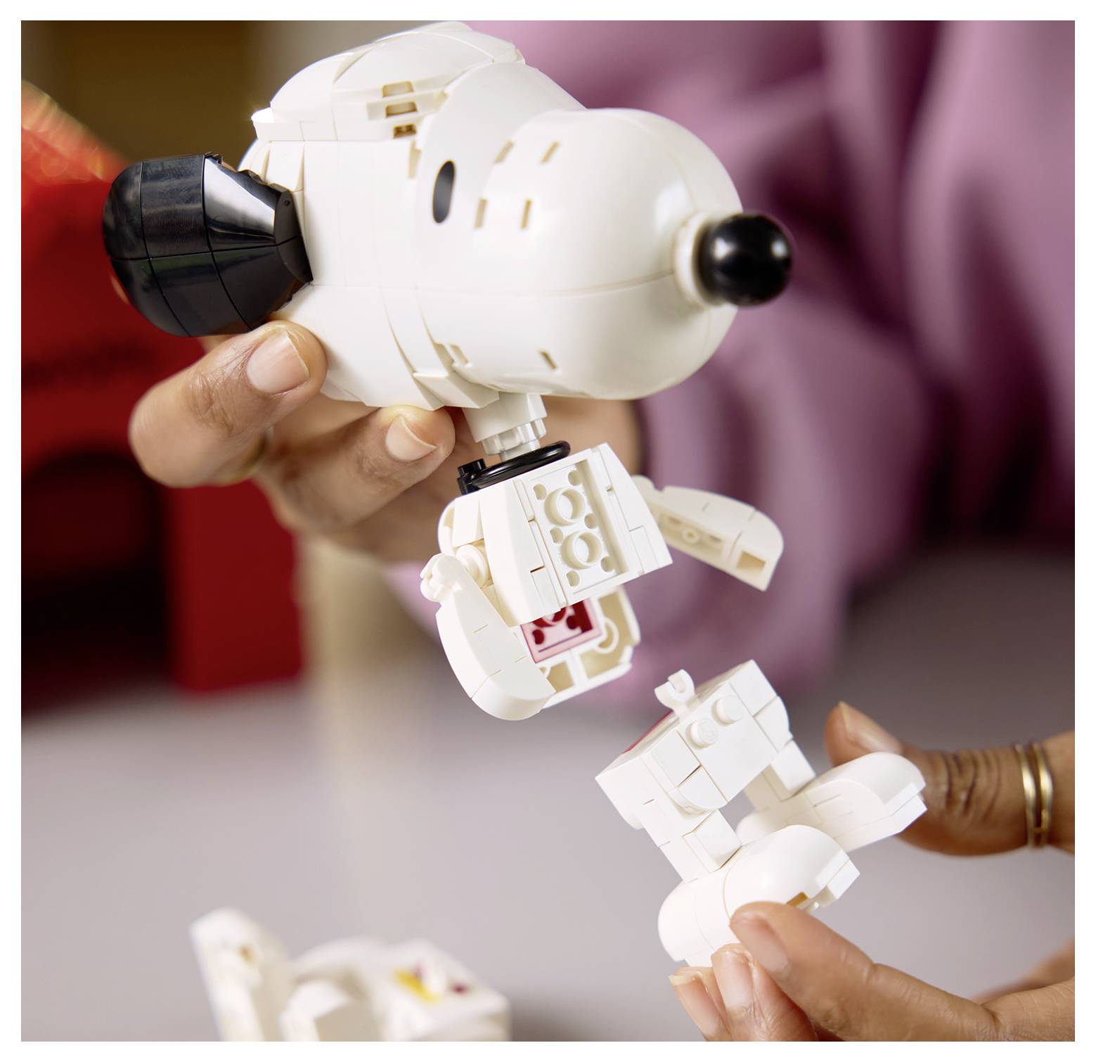 Hände, die eine weiße LEGO-Snoopy-Figur zusammenbauen, mit sichtbaren abgetrennten Teilen.