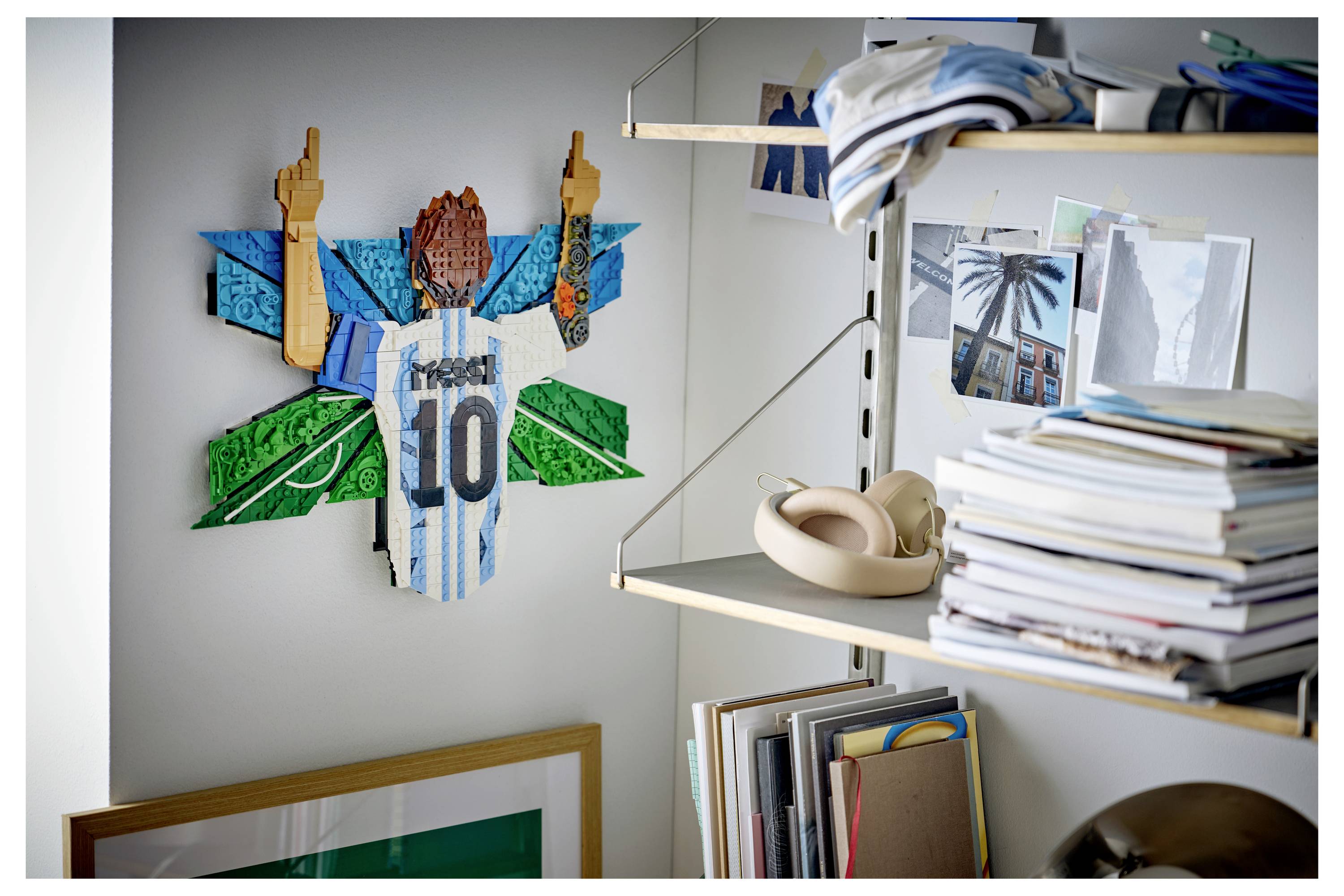 Eine an der Wand montierte Fußball-Trikot-Collage mit der Nummer 10 hängt neben Regalen mit Büchern, Zeitschriften und gefalteter Kleidung in einem ordentlichen Zimmer.