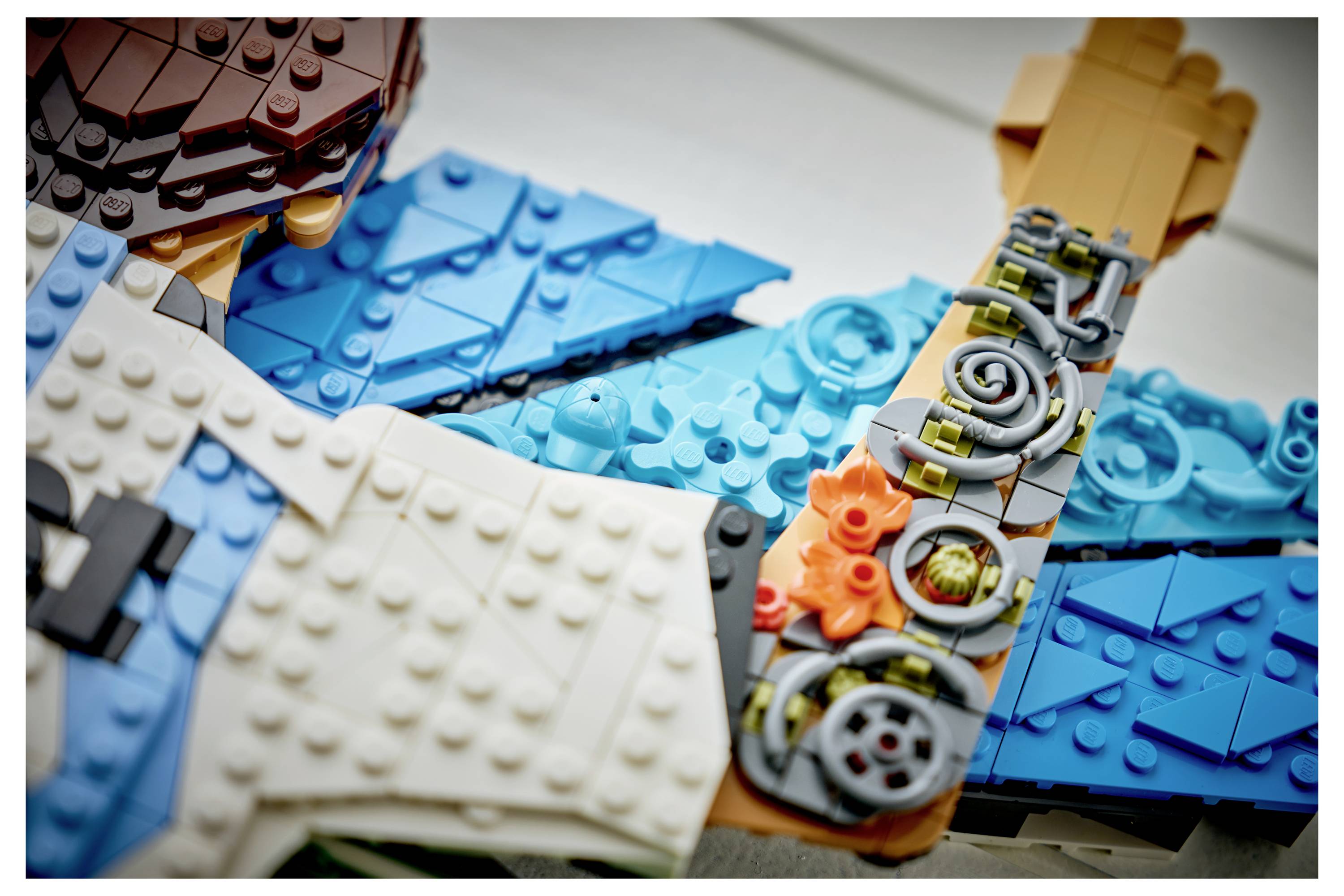 Nahaufnahme von sortierten LEGO-Teilen und Minifiguren-Komponenten, die auf einem Tisch angeordnet sind und blaue, weiße, braune und orangefarbene Steine sowie Zahnräder zeigen.