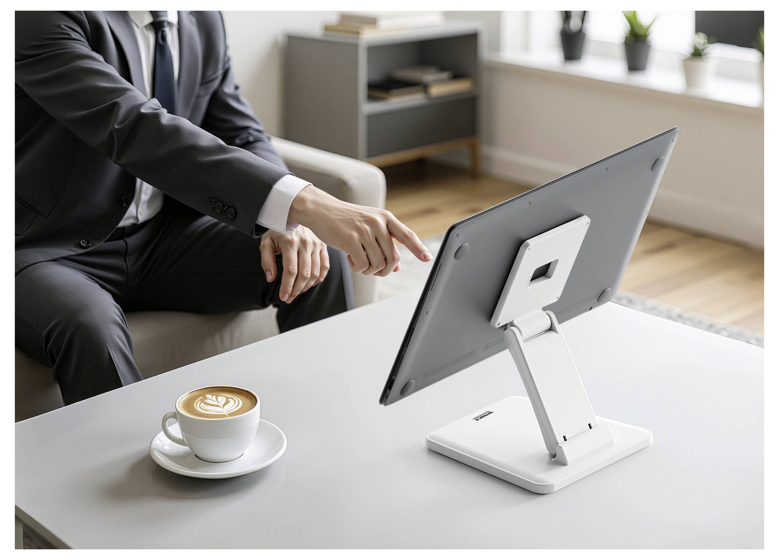 Geschäftsperson im Anzug zeigt auf einen Desktop-Monitor auf einem weißen Tisch neben einer Tasse Kaffee in einer Büroumgebung.