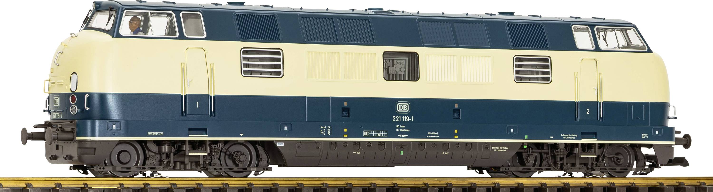 Seitenansicht einer creme- und dunkelgrünen Diesellok auf Eisenbahngleisen, mit einem sichtbaren Lokführer in der Kabine.