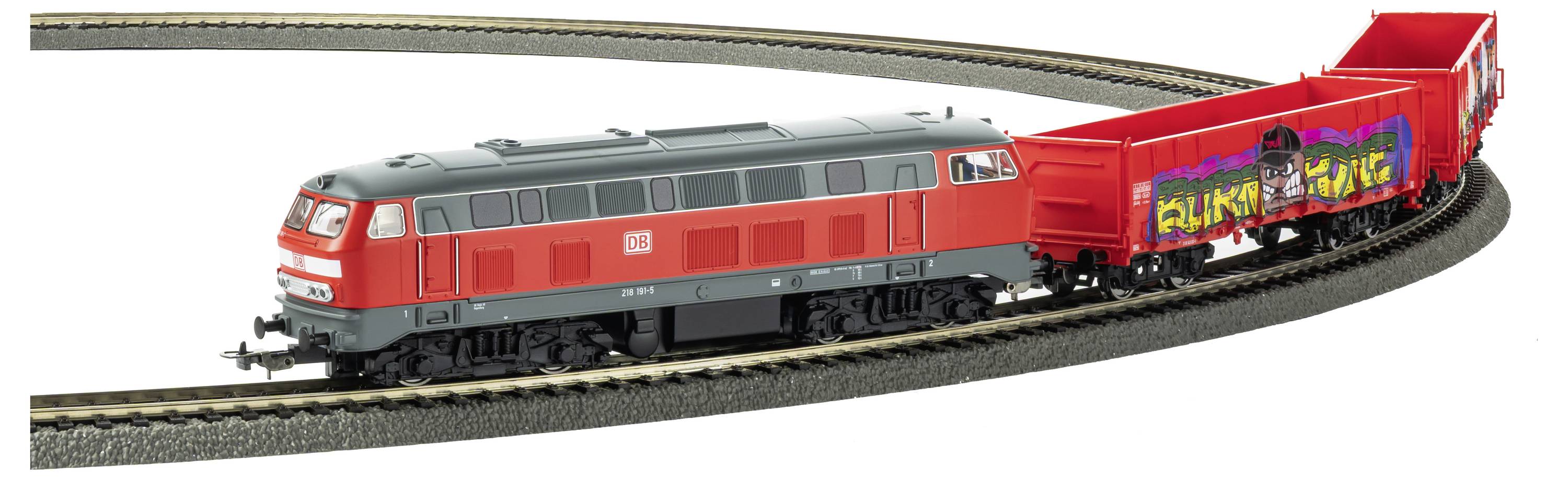 Rote Modelleisenbahn zieht einen rot besprühten Güterwagen auf einem gebogenen Miniaturgleis.