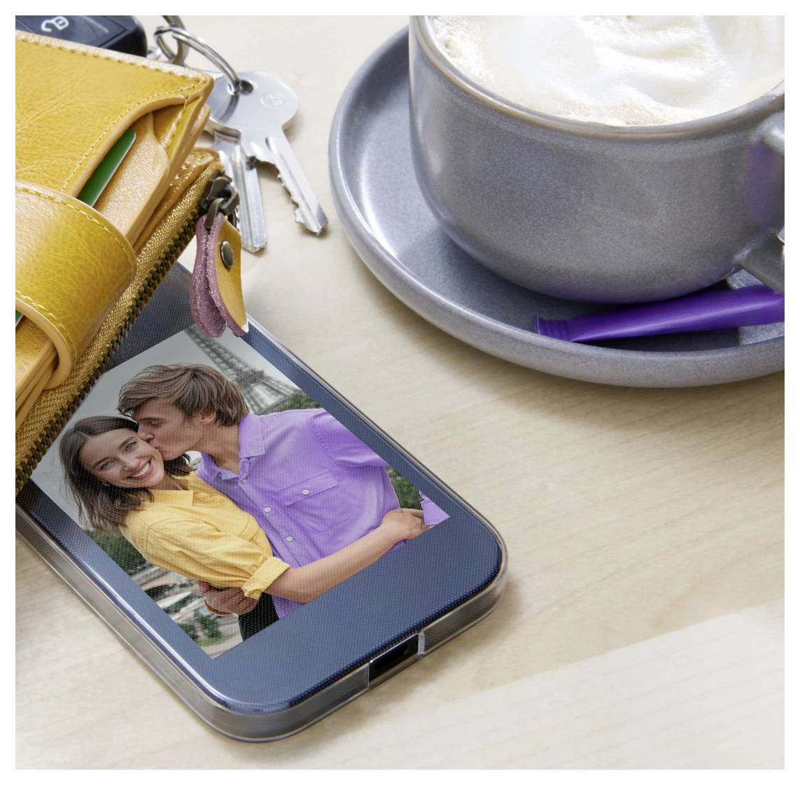 Smartphone, auf dem ein Paar-Foto angezeigt wird, neben einem gelben Portemonnaie, Schlüsseln und einer Tasse Kaffee auf einem Tisch.