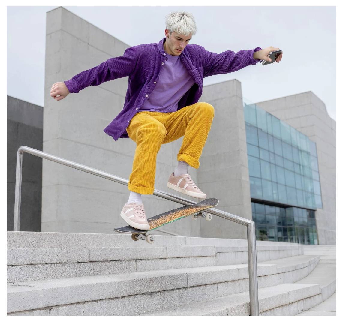 Skateboarder in violetter Jacke und gelber Hose, der auf einem Handlauf eine Outdoor-Betontreppe neben einem modernen Gebäude entlangschleifen.