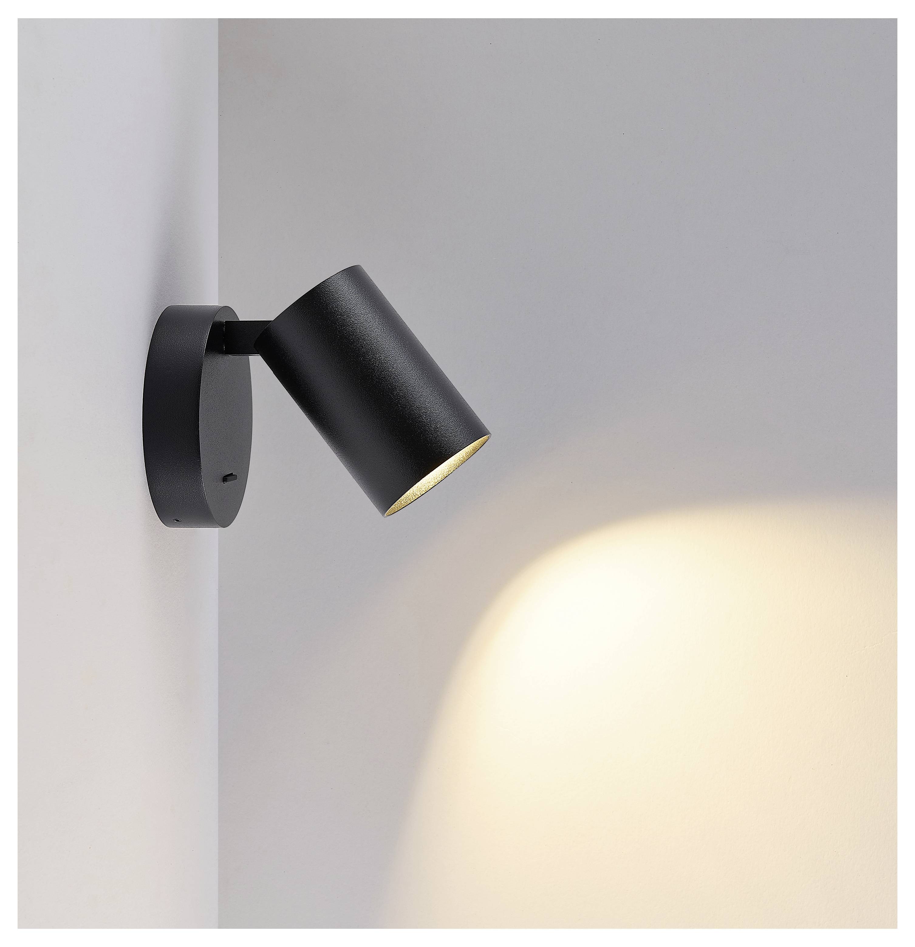 Schwarzer verstellbarer Wandstrahler wirft einen warmen Lichtstrahl auf eine schlichte hellgraue Wand.
