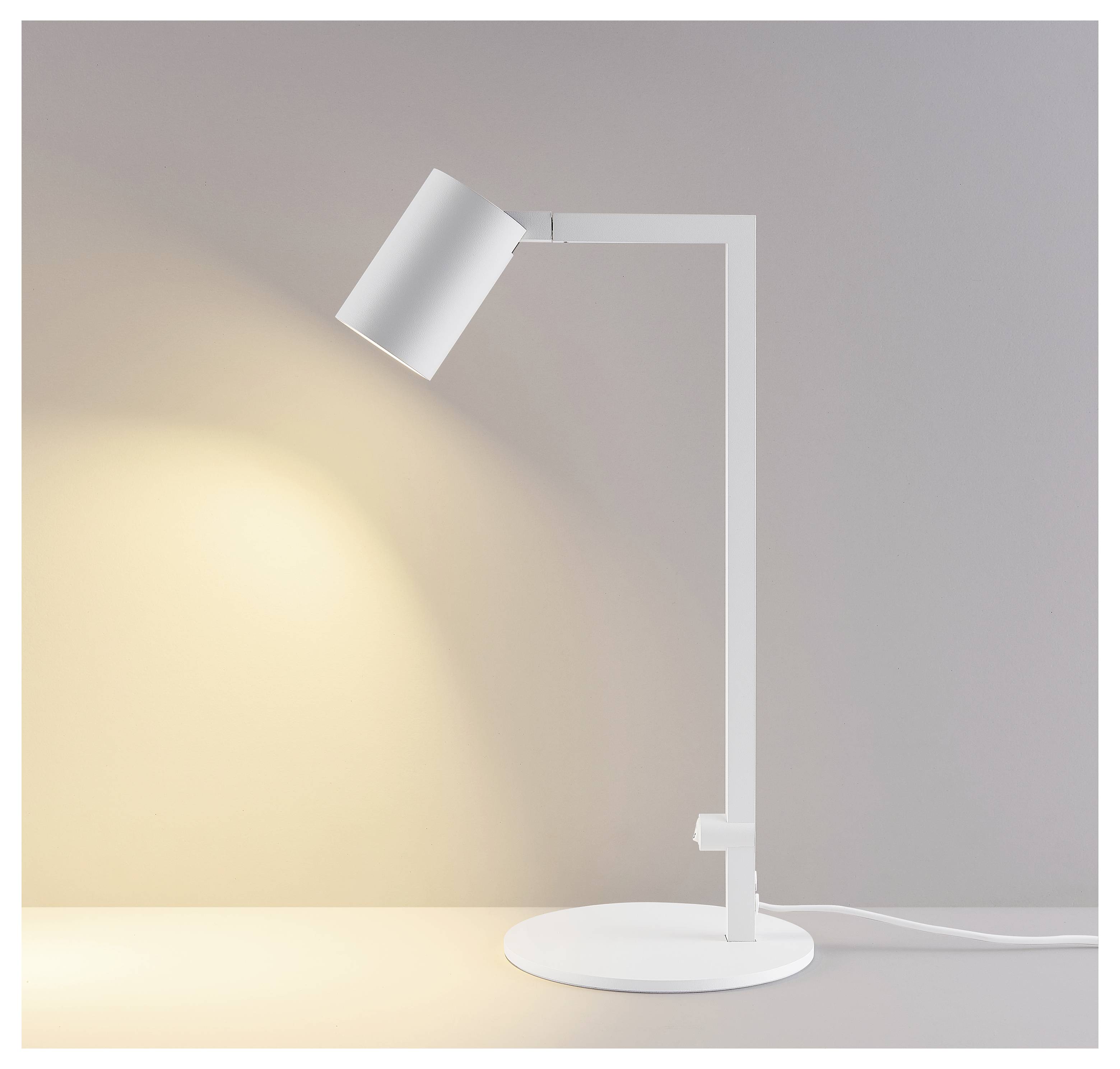 Minimale weiße Schreibtischlampe auf rundem Sockel, die warmes Licht auf eine schlichte Wand wirft.