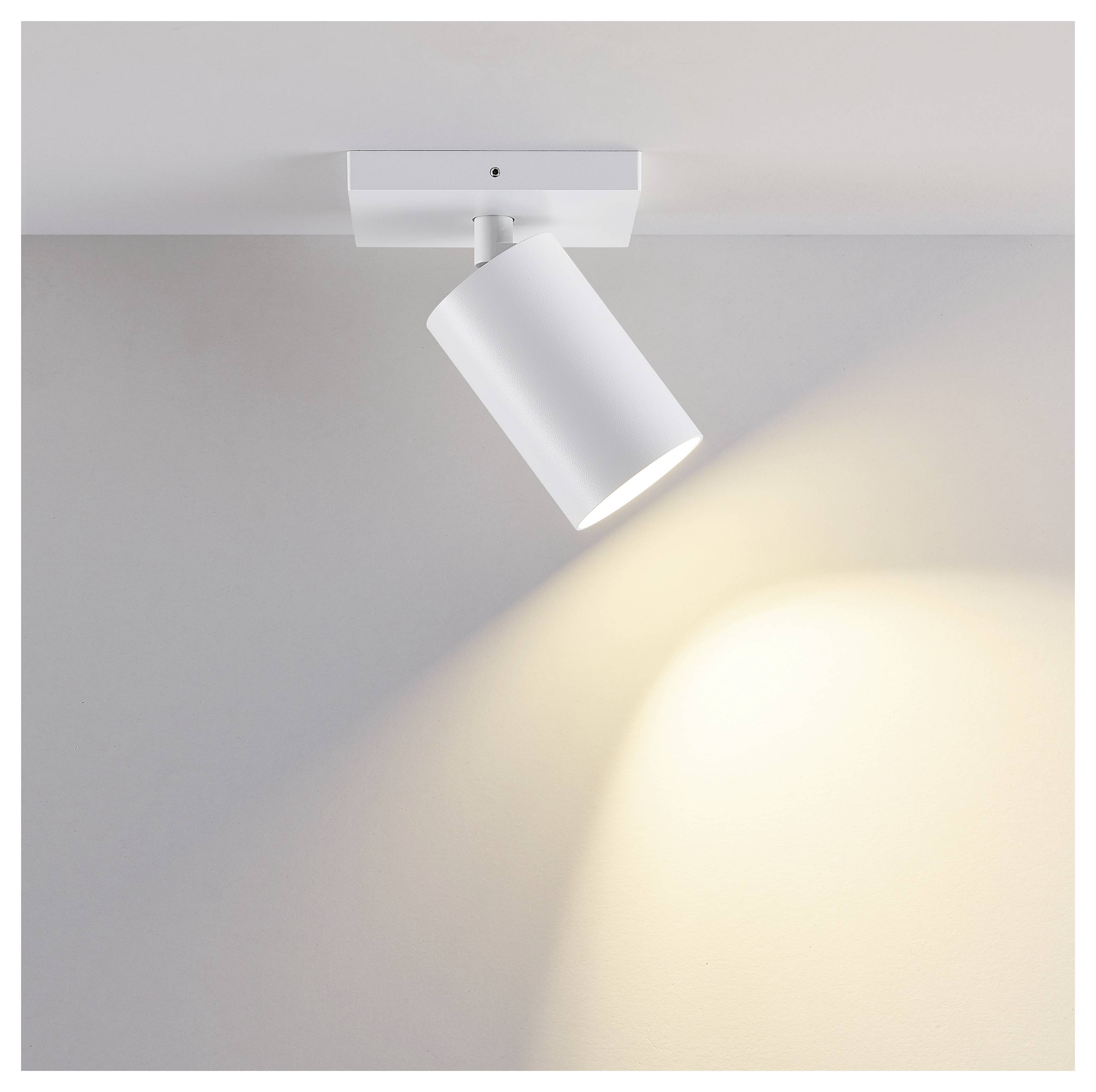 Weißer verstellbarer Deckenspot mit warmem Lichtstrahl auf einer grauen Wand