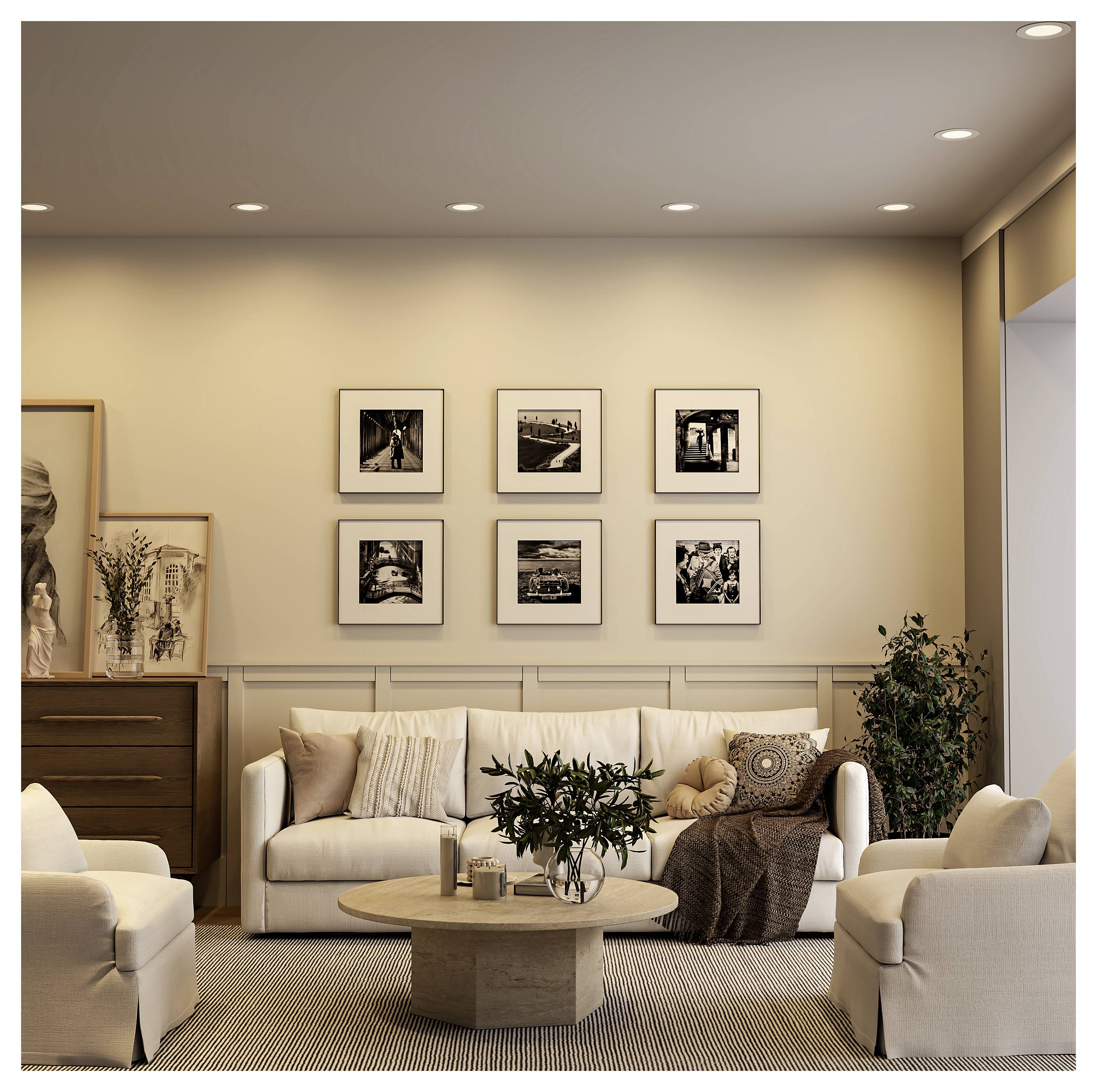 Ein gemütliches modernes Wohnzimmer mit einem cremefarbenen Sofa, Sesseln, rundem Couchtisch, gerahmten Wandbildern und warmem Einbauleuchten.