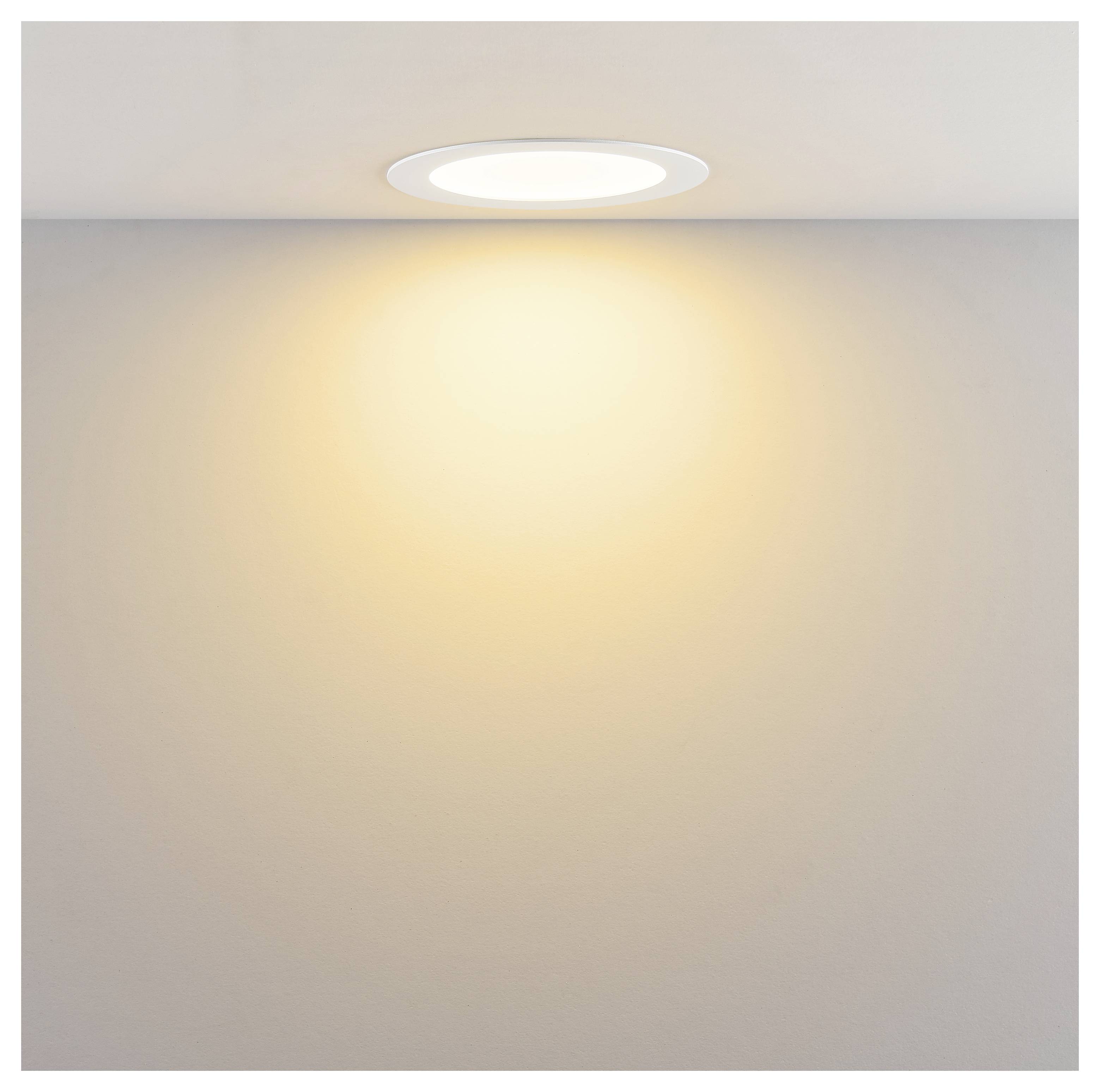 In die Decke eingelassene Leuchte, die einen warmen, kreisförmigen Lichtkegel auf eine schlichte Wand wirft.