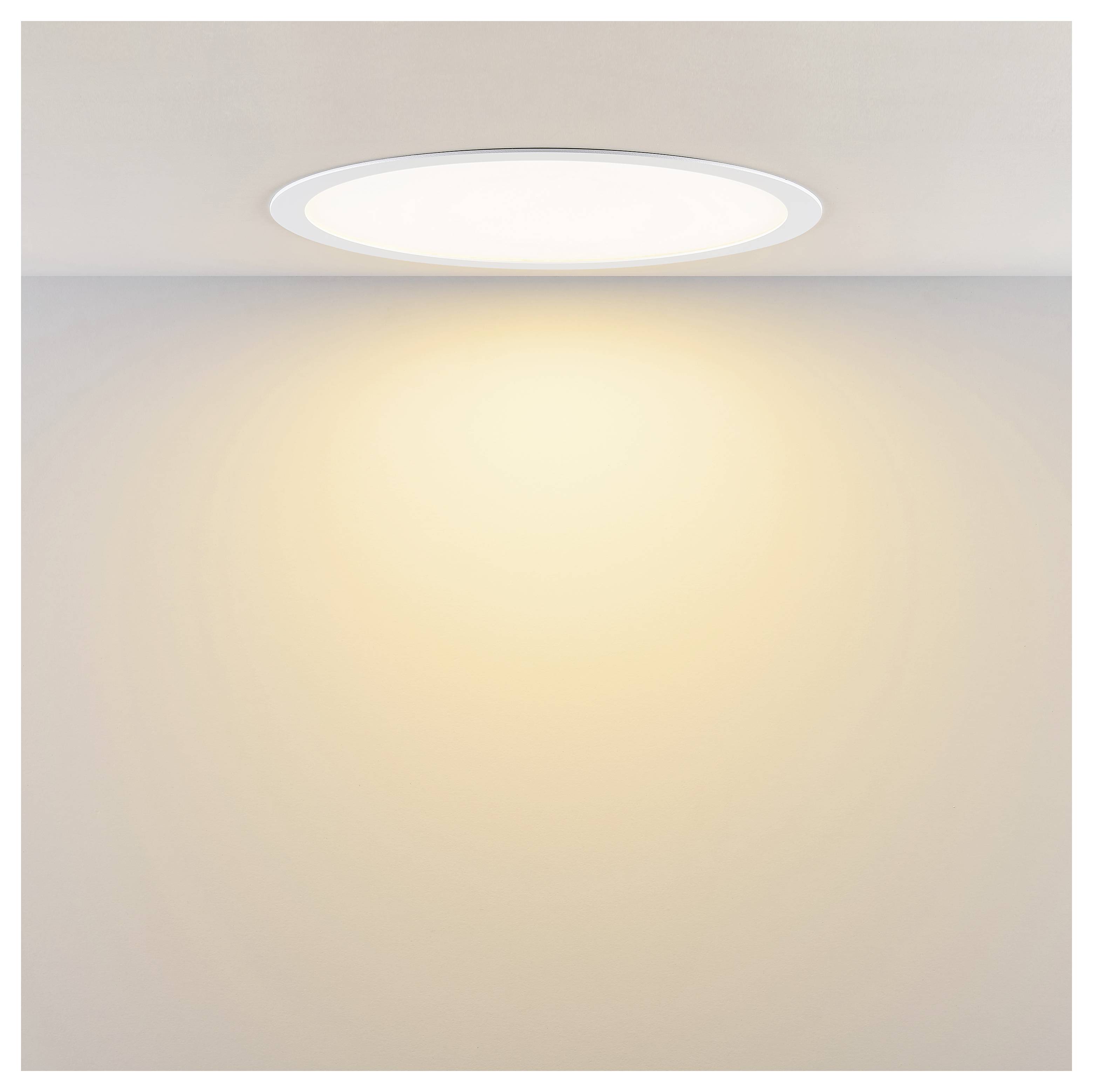 In der Decke eingelassene runde Leuchte, die einen warmen Glanz auf eine schlichte Wand wirft.