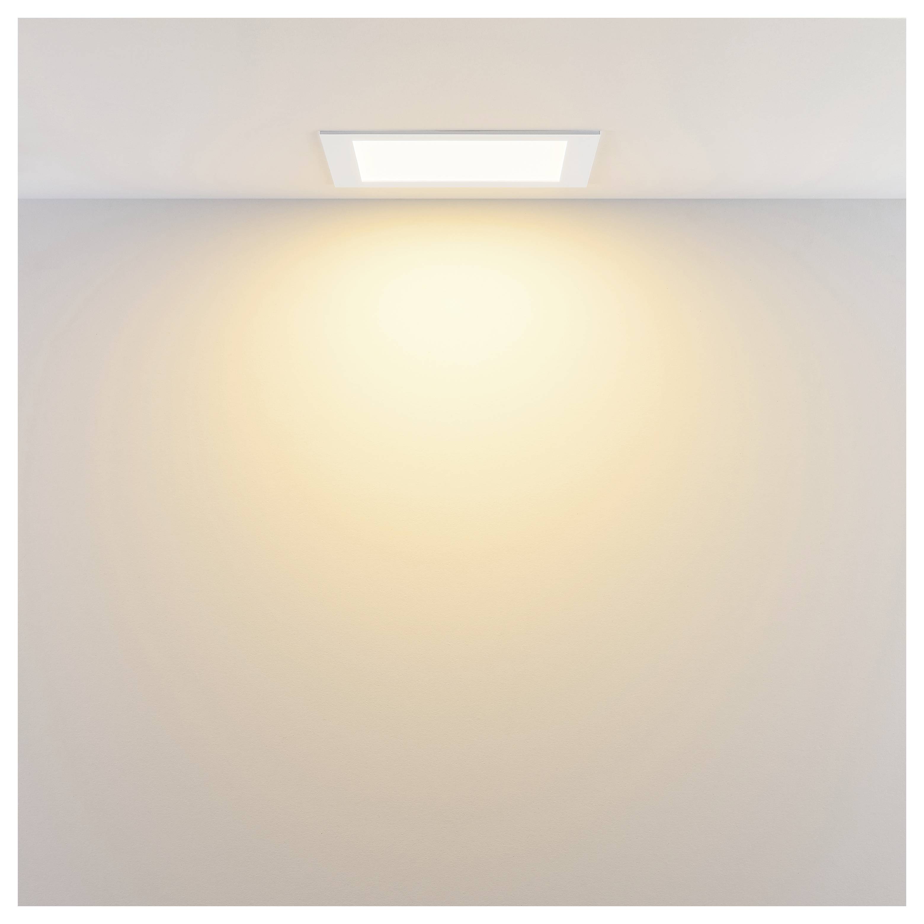 Eine in der Decke eingelassene Leuchte, die ein warmes Licht auf eine leere Wand wirft.
