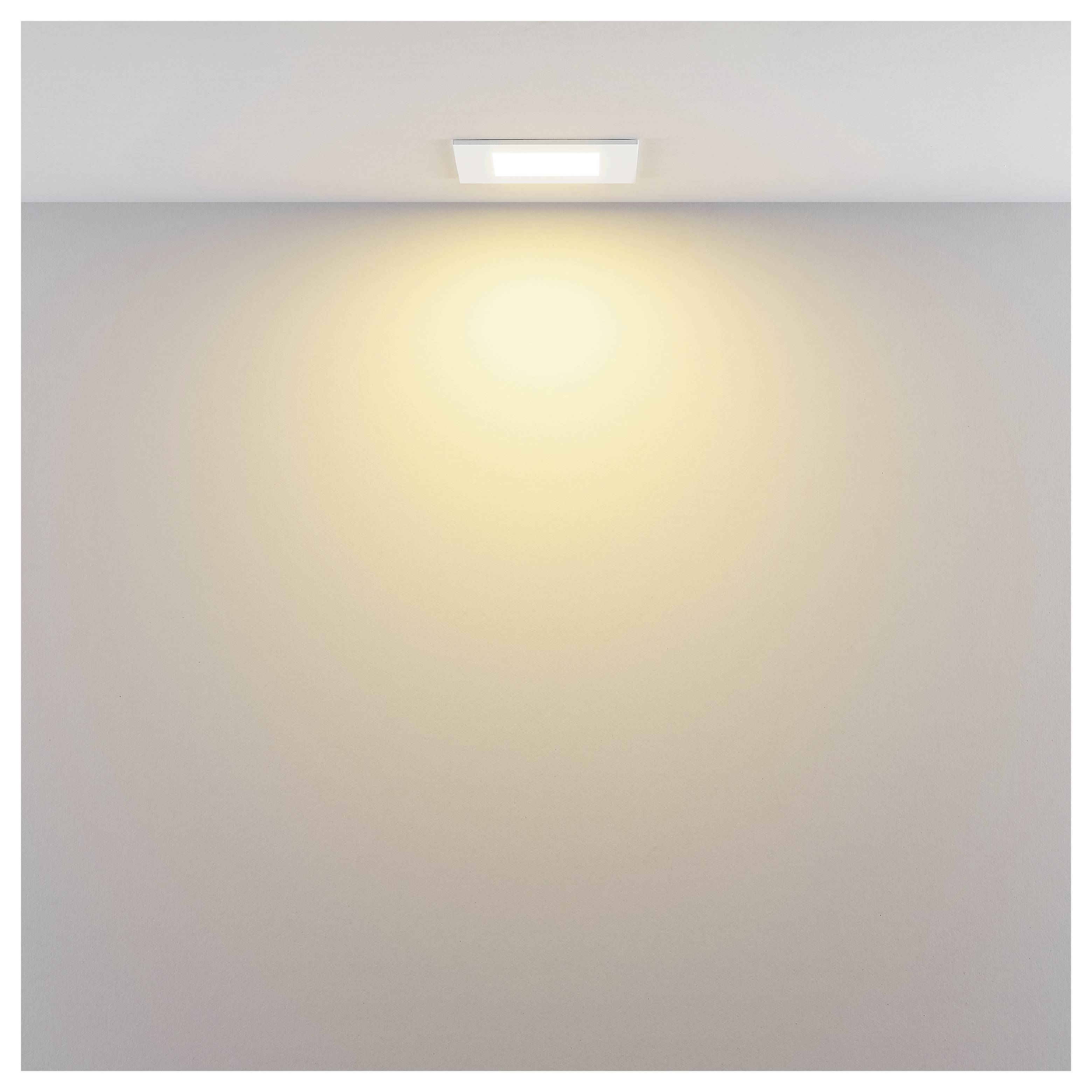 An der Decke montierte quadratische Einbauleuchte, die ein warmes Licht auf eine leere weiße Wand wirft.