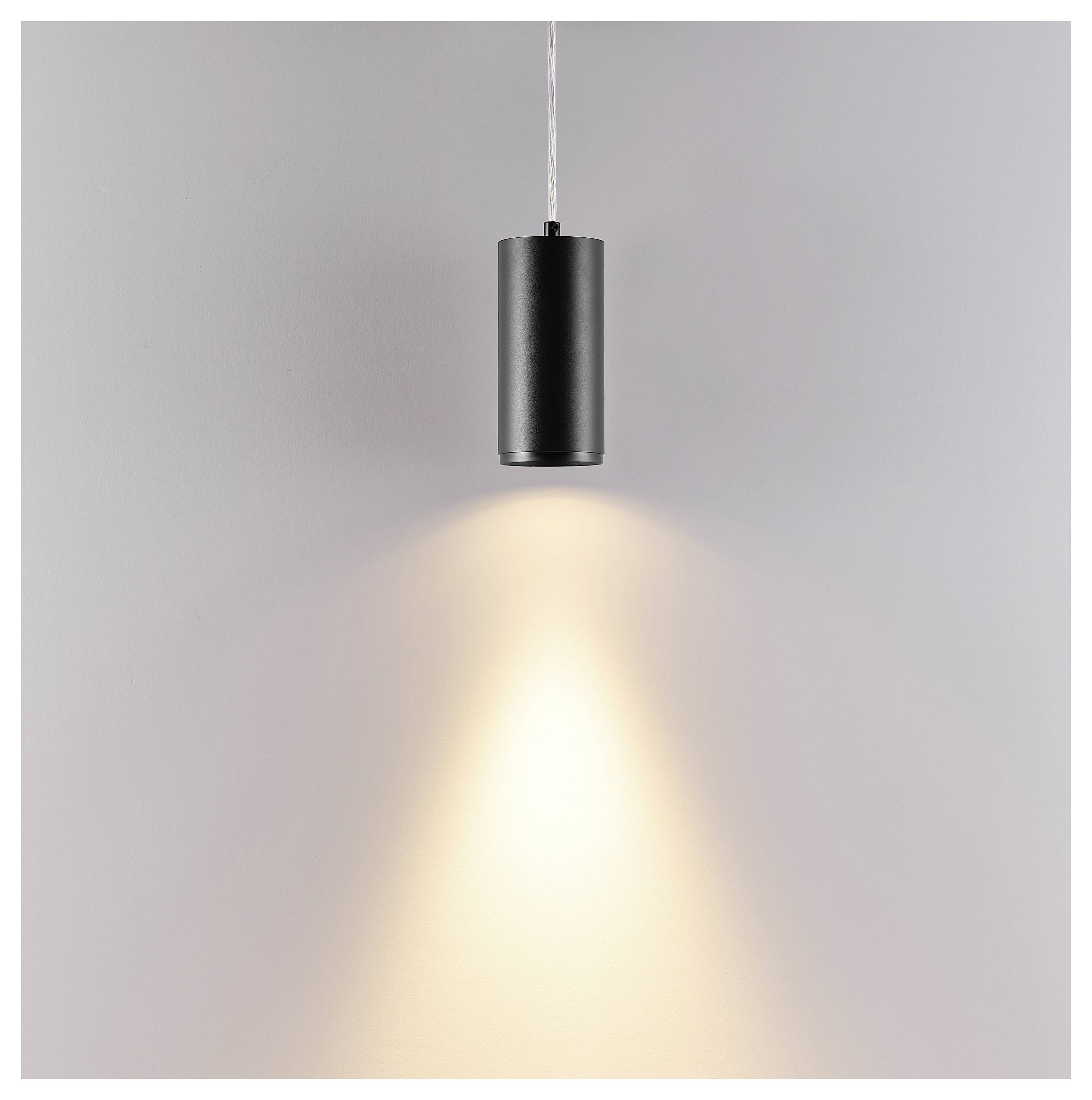 Schwarze zylindrische Pendelleuchte, die einen warmen Lichtkegel auf eine schlichte Wand wirft.