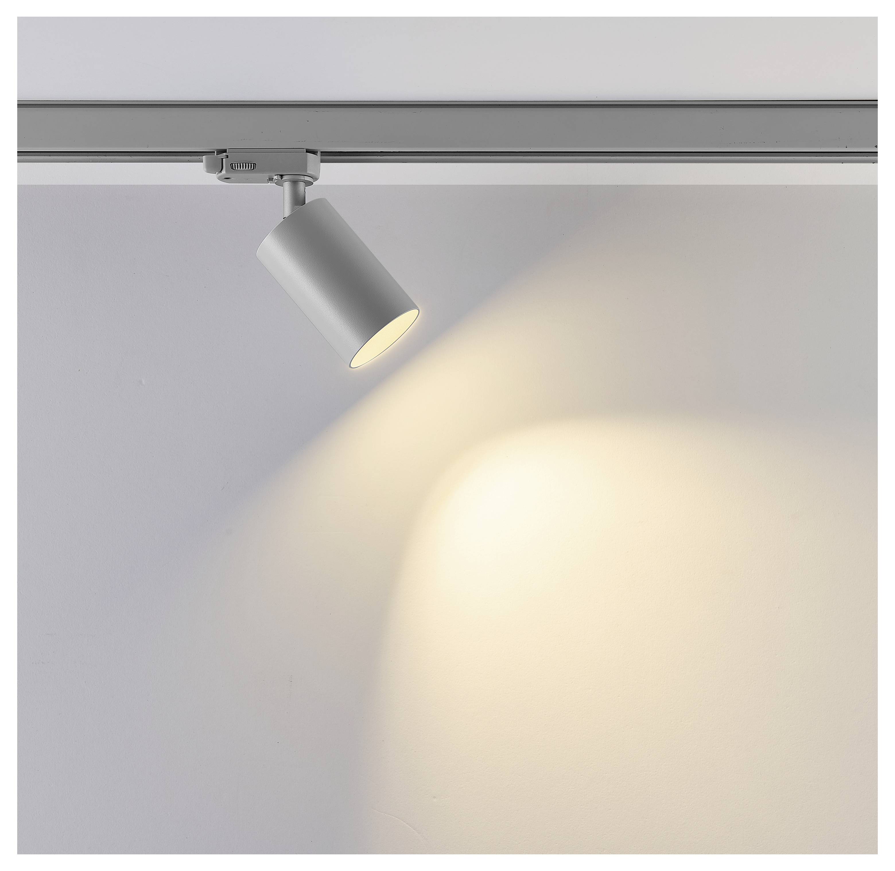 Silberne Schienenstrahler an einer Deckenleiste, nach unten gerichtet und wirft ein warmes Spotlight auf eine leere Wand.