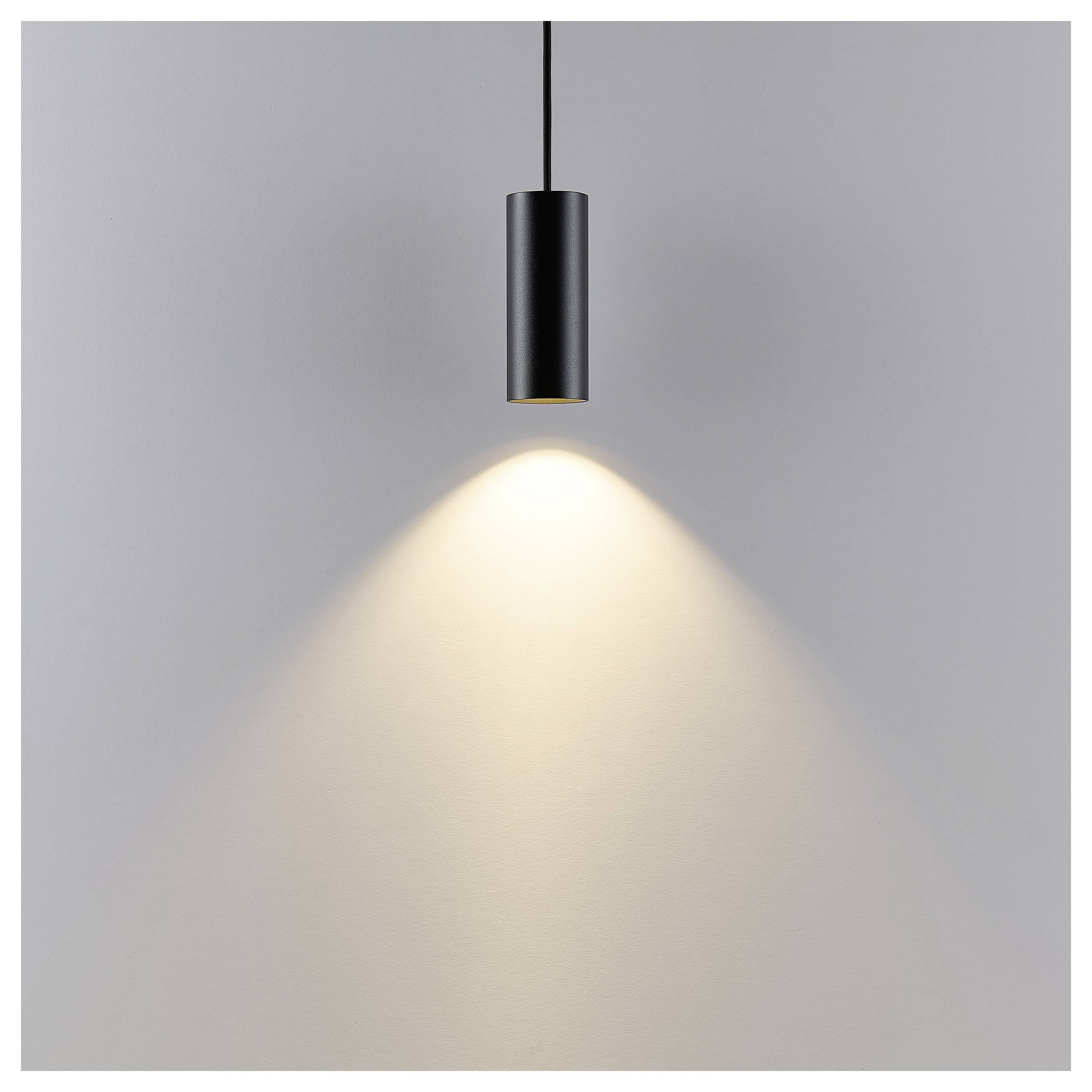 Schwarze zylindrische Pendelleuchte, die einen warmen Lichtkegel auf eine schlichte graue Wand wirft.