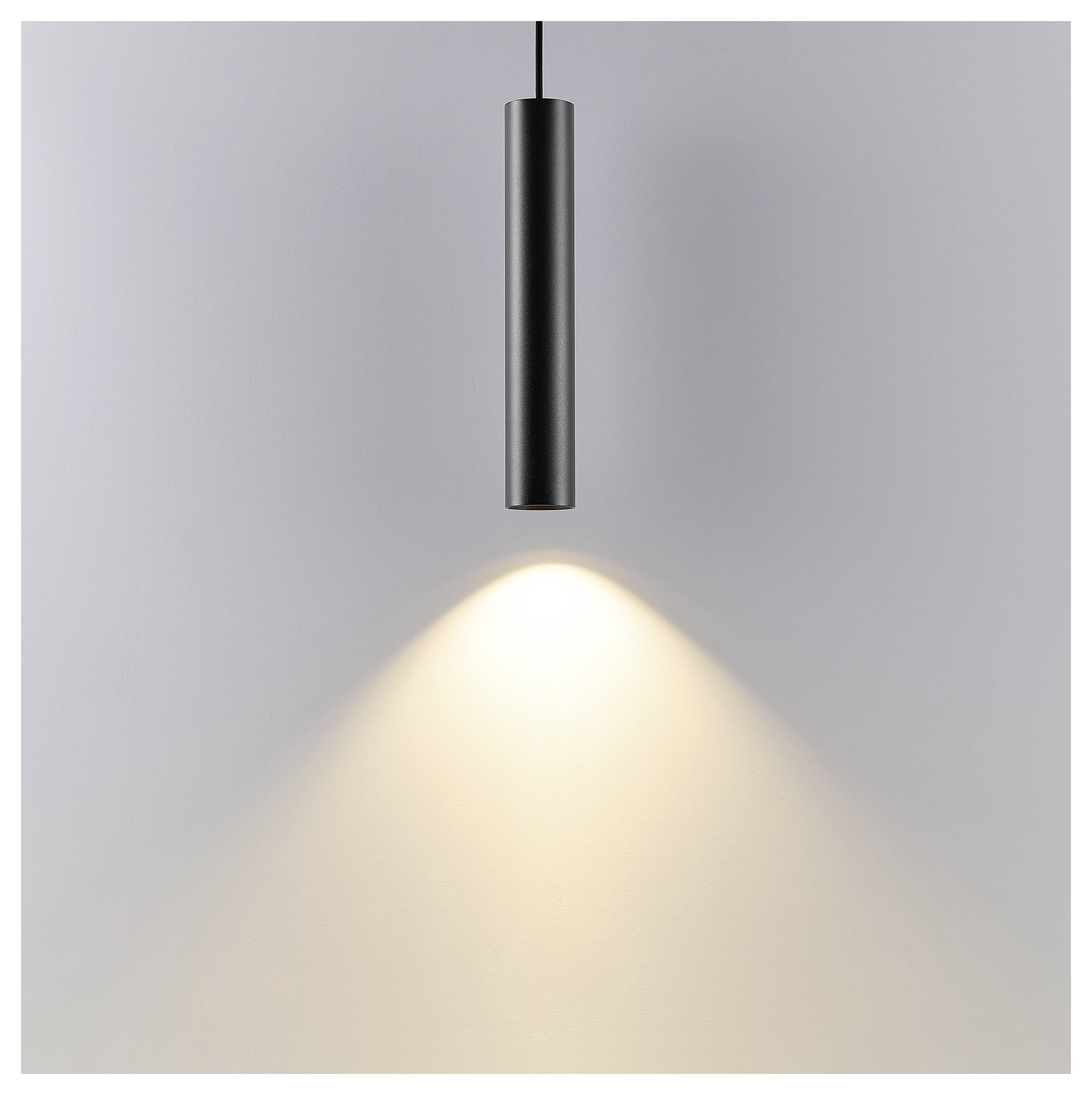 Schwarze zylindrische Pendelleuchte, die von der Decke hängt und einen warmen Lichtkegel auf eine schlichte graue Wand wirft.