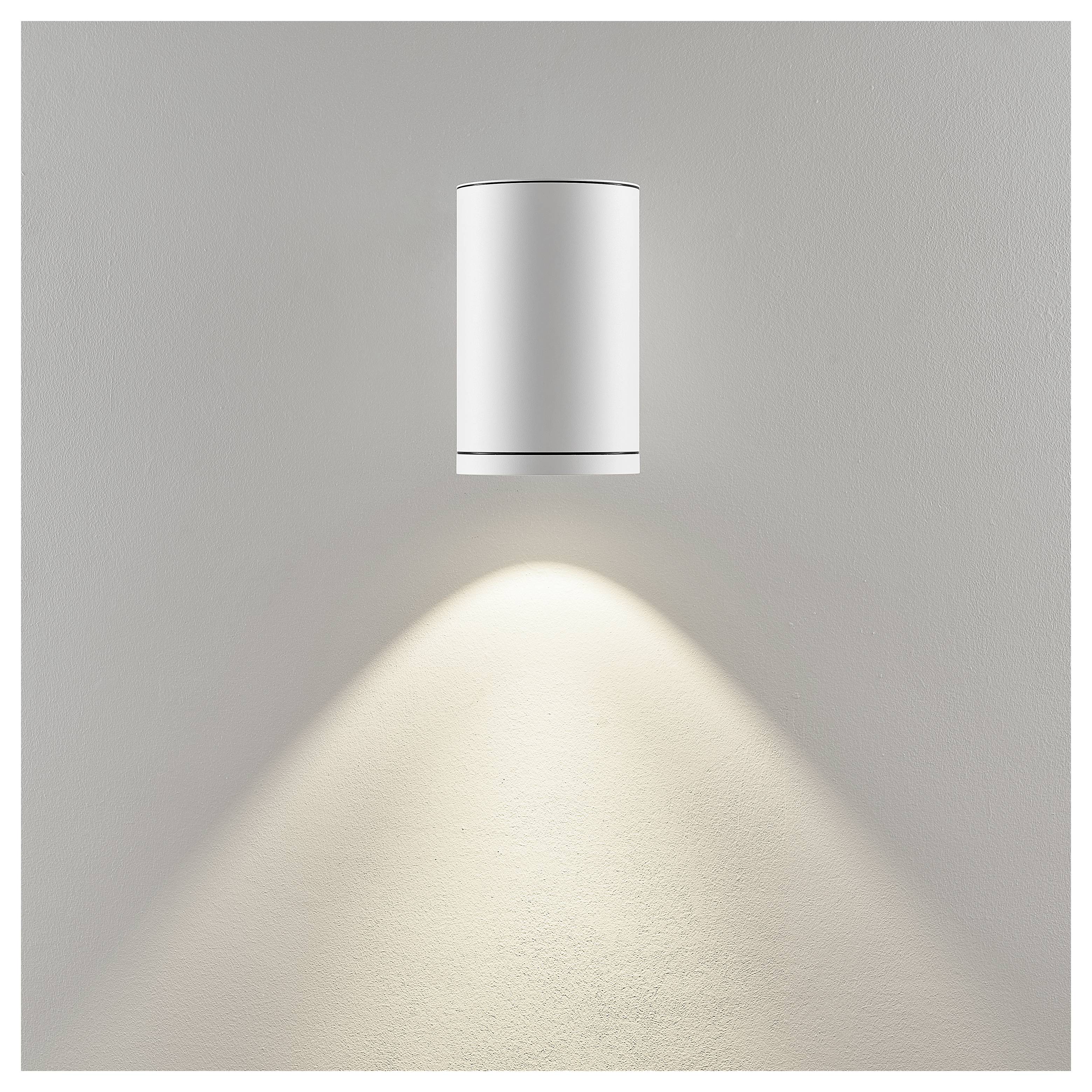 Moderne zylindrische Wandleuchte, die weiches Licht nach unten auf eine graue Wand wirft.