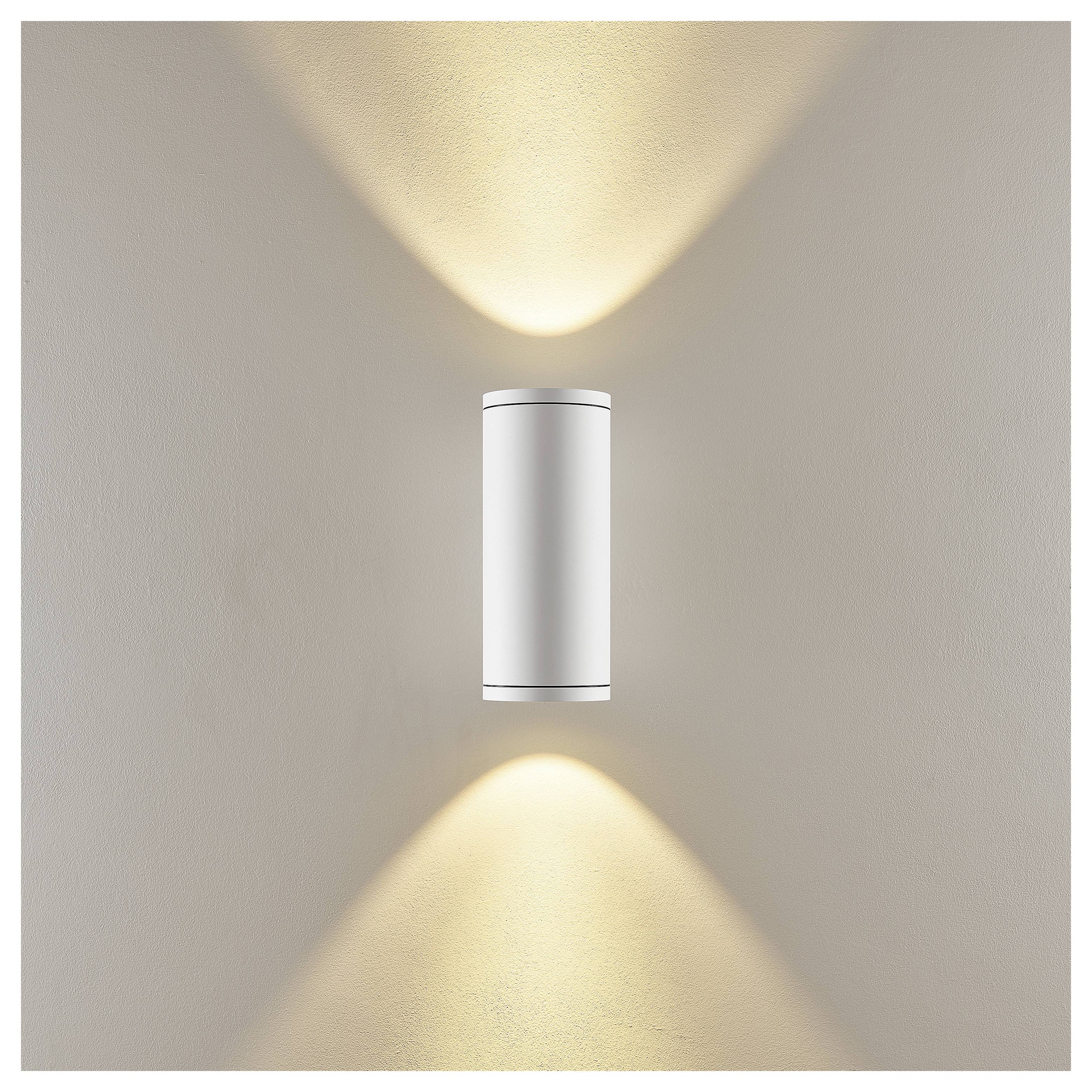 Moderne Wandleuchte mit weißem zylindrischem Körper, die warme Lichtstrahlen nach oben und unten auf einer beigefarbenen Wand wirft.