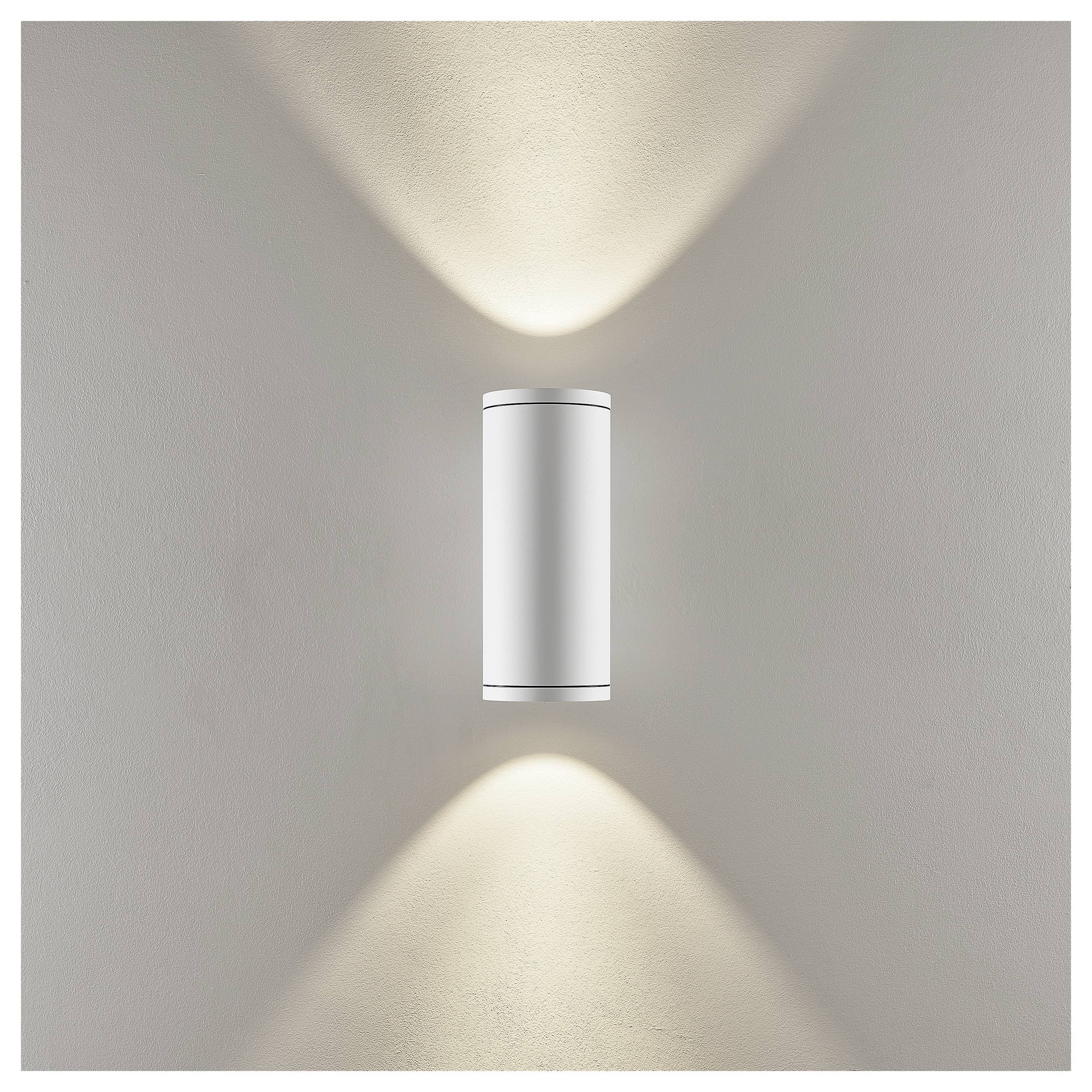 Wandleuchte mit minimalem zylindrischem Design, das warmes Licht nach oben und unten auf eine beige Wand wirft.
