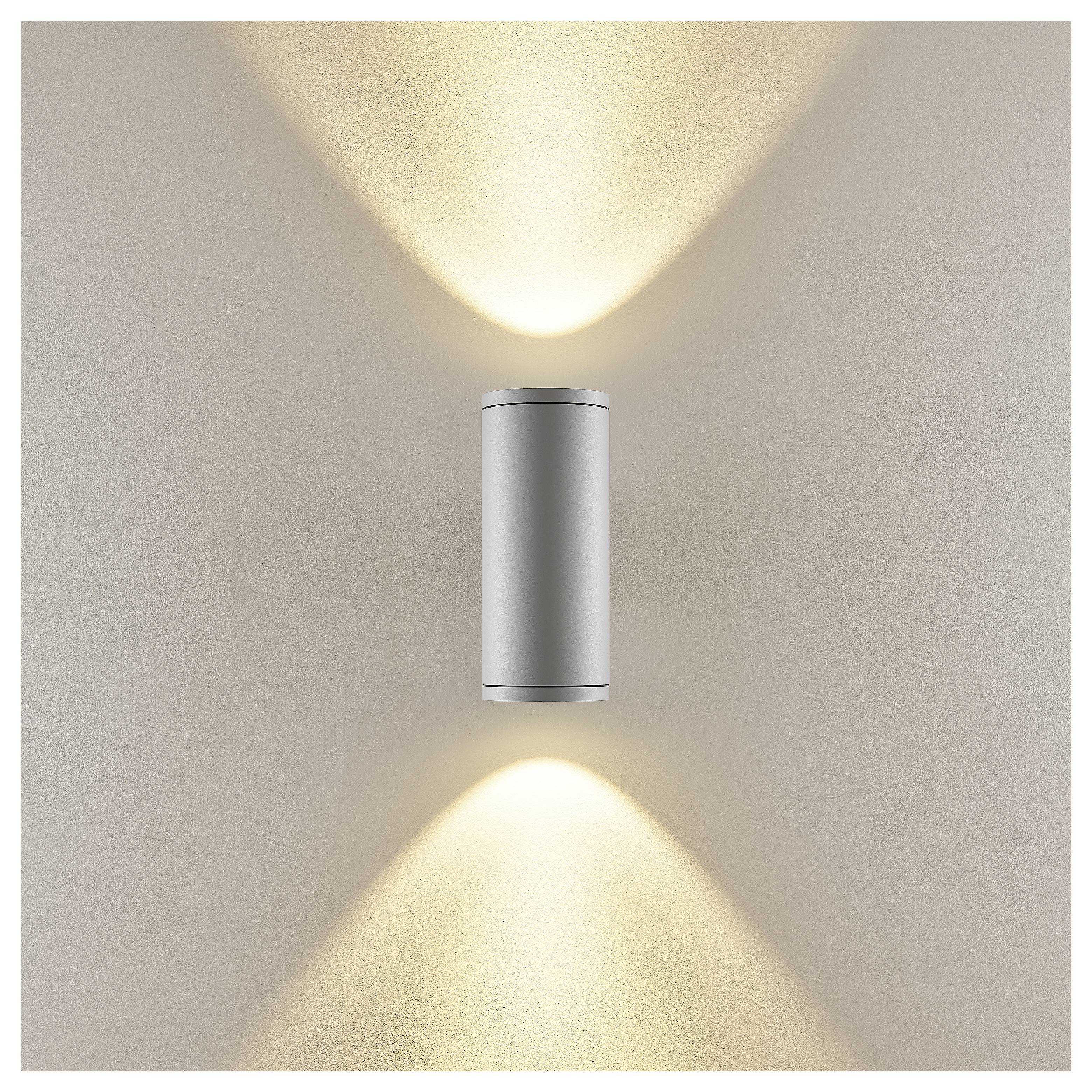 Moderne zylindrische Wandleuchte, die warmes Licht sowohl nach oben als auch nach unten auf eine beige Wand wirft