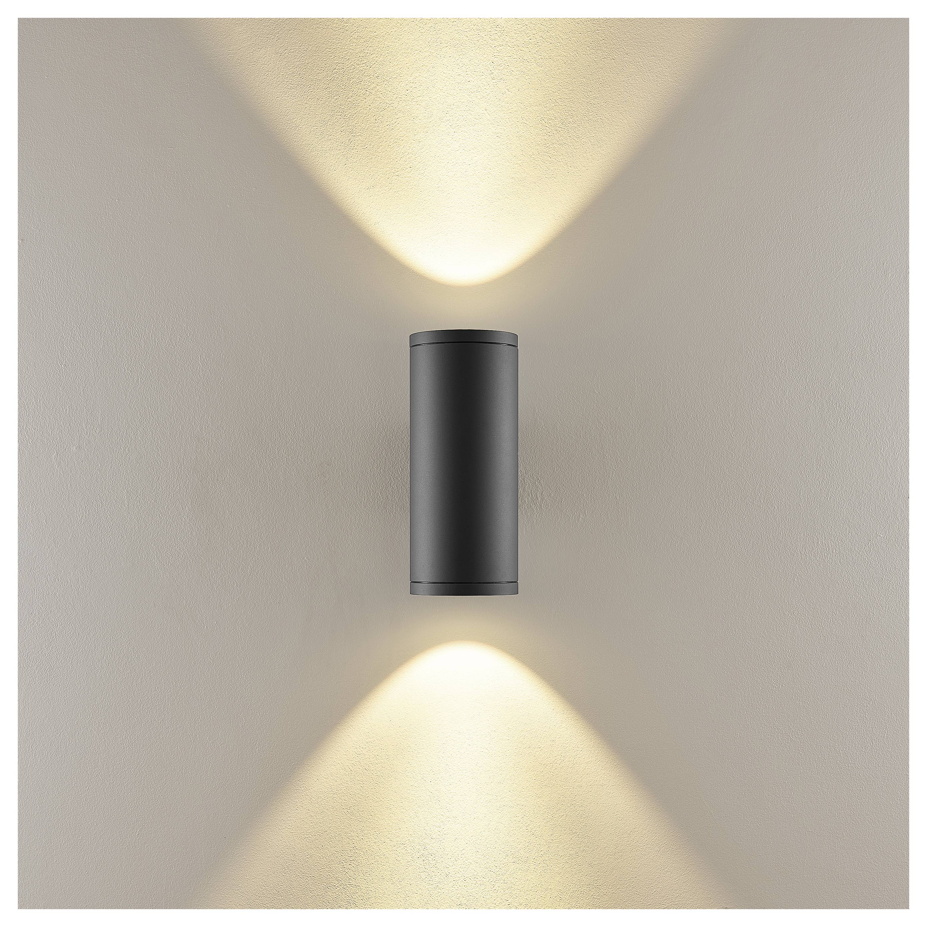 Schwarze zylindrische Wandleuchte wirft warmes Licht auf und ab auf einer beigefarbenen Wand.