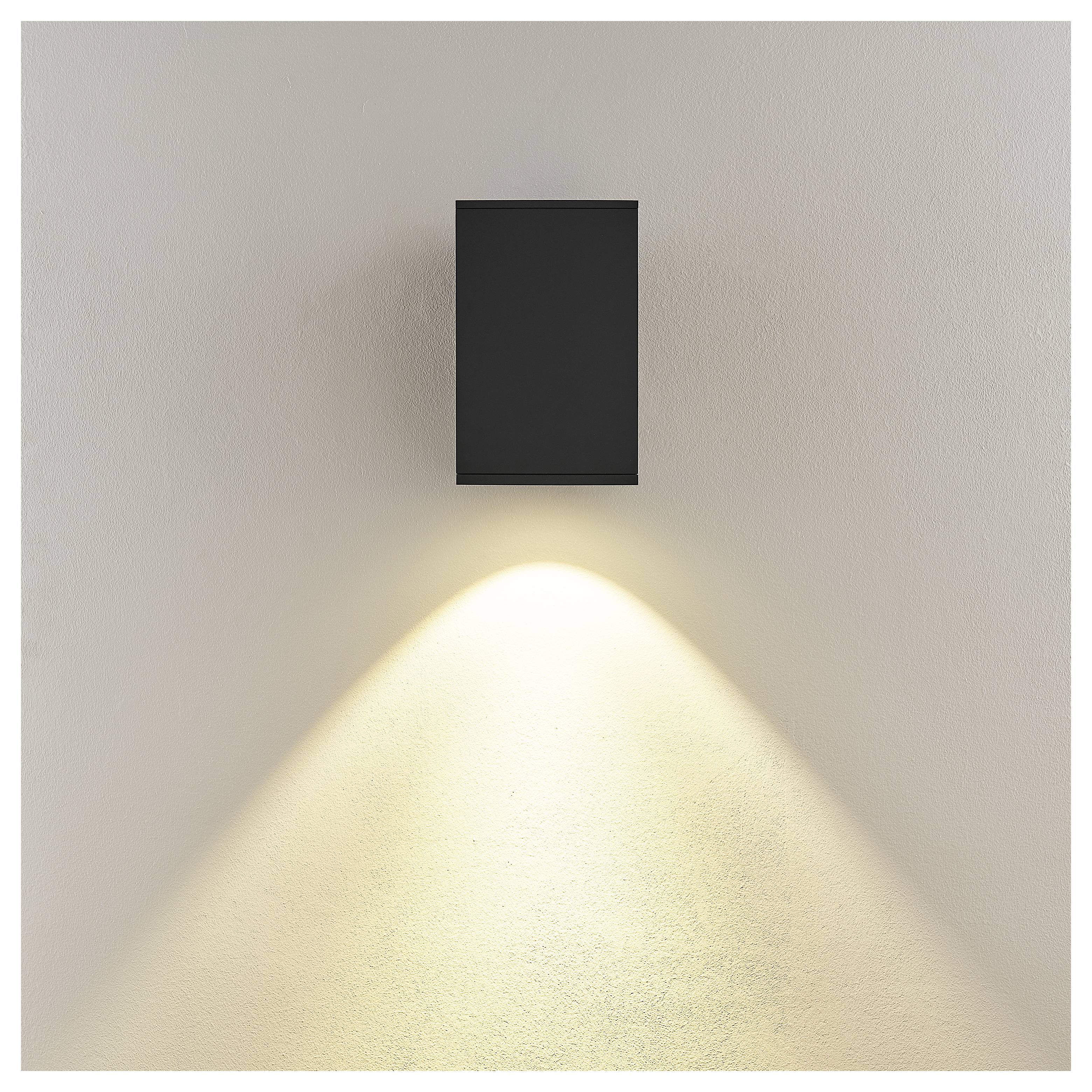 Schwarze Wandleuchte, die einen warmen Lichtkegel auf eine beige Wand wirft.
