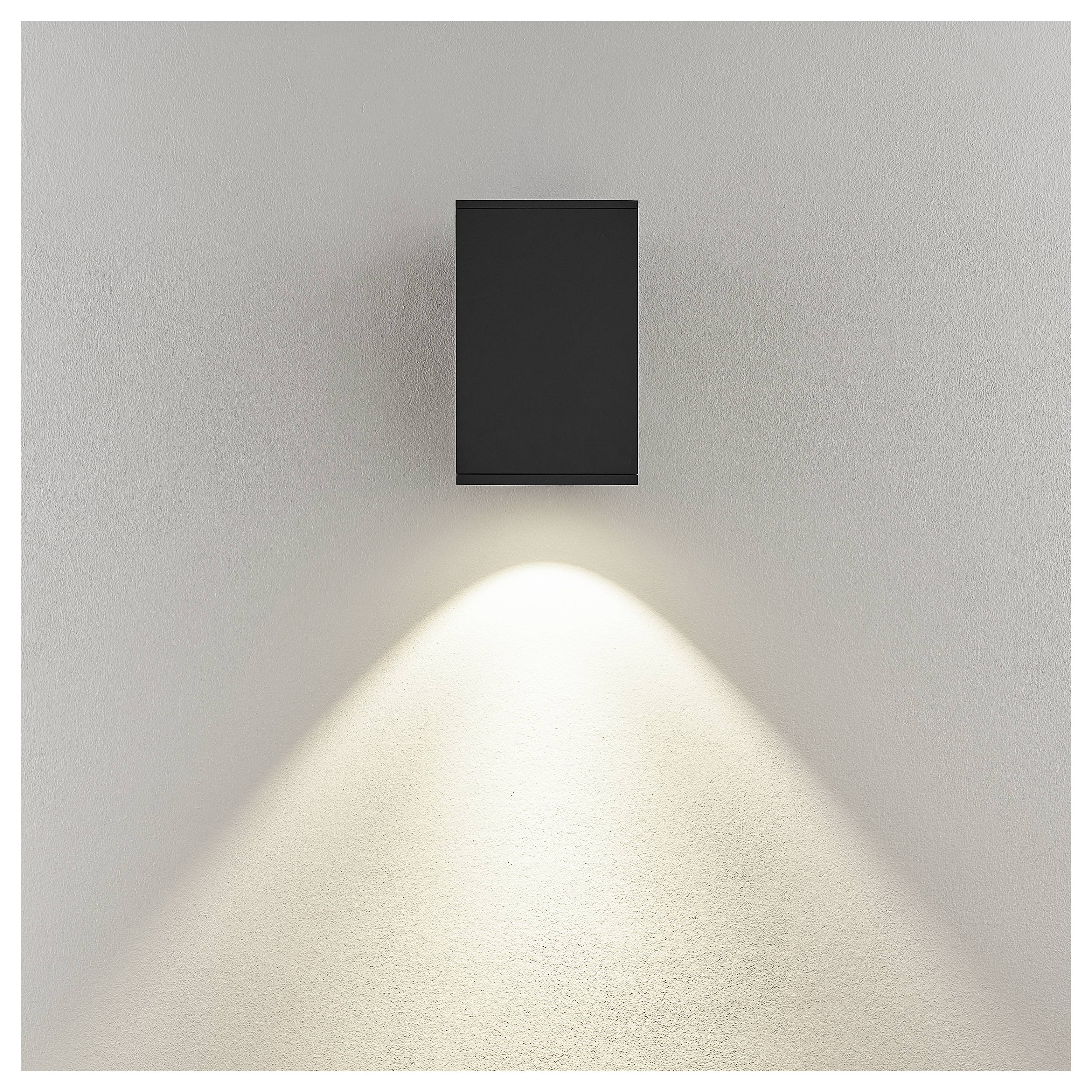Schwarze wandmontierte Leuchte, die einen breiten Abwärtsstrahl auf eine schlichte hellfarbige Wand wirft.