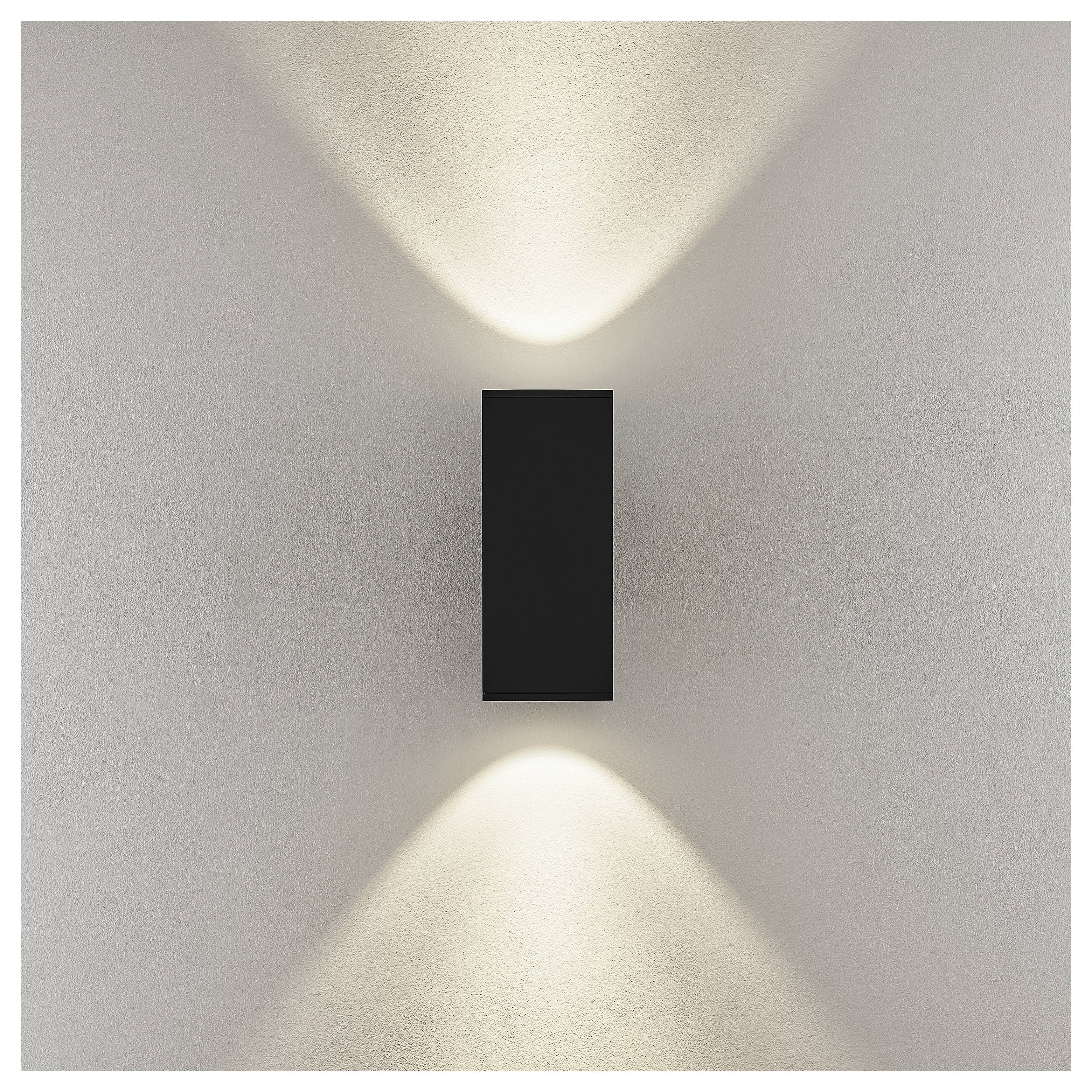 Minimalistische Wandleuchte mit einem schwarzen rechteckigen Gehäuse, das weiches Licht nach oben und unten auf eine weiße Wand wirft.