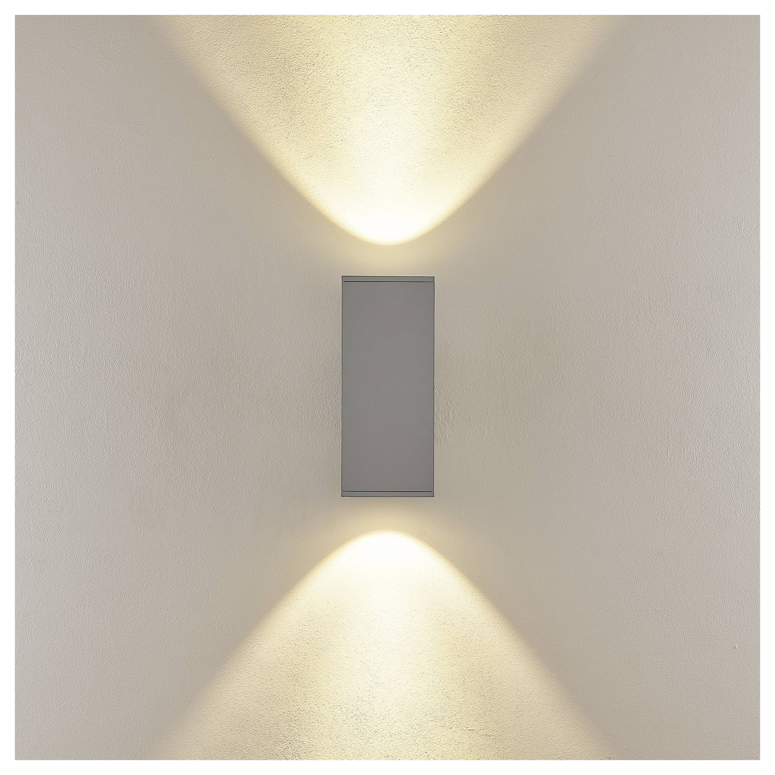 Moderne Wandleuchte, die zwei symmetrische Lichtstrahlen in warmem Licht oberhalb und unterhalb einer schmalen rechteckigen Leuchte an einer schlichten Wand wirft.