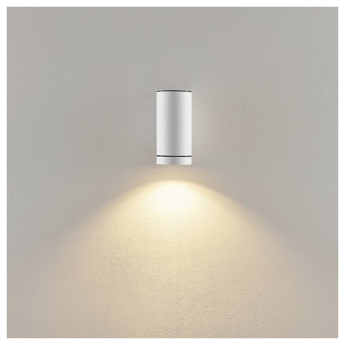 Minimale weiße Wandleuchte, die einen warmen, nach unten gerichteten Lichtkegel auf eine schlichte beigefarbene Wand wirft.