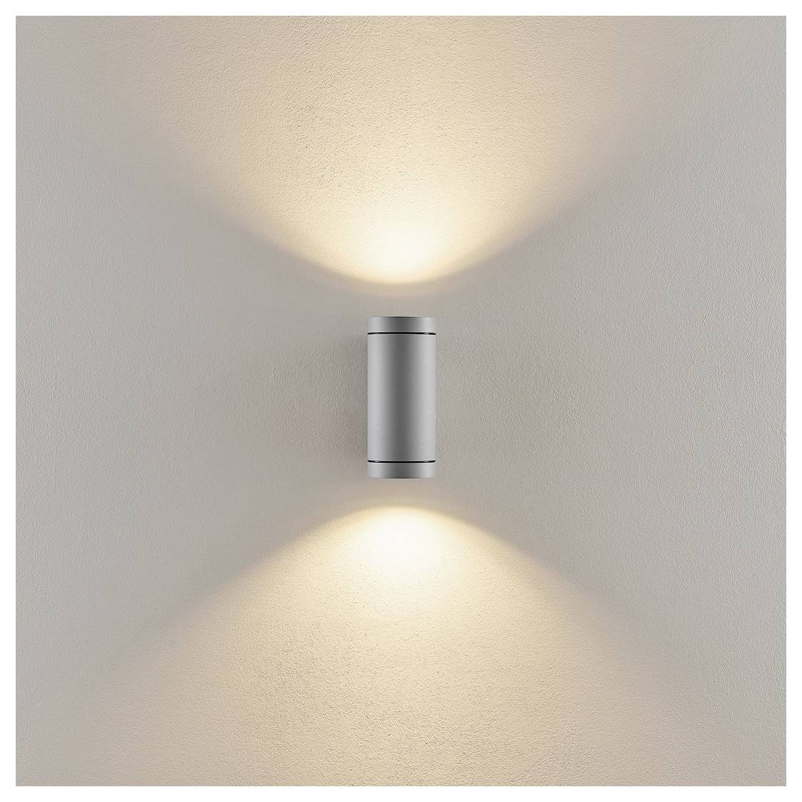 Eine minimalistische Wandleuchte, die warmes Licht nach oben und unten auf eine beige Wand wirft.