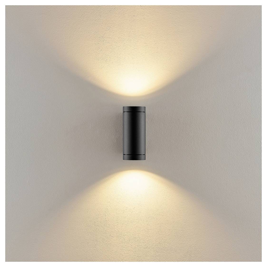 Schwarze zylindrische Wandleuchte, die warmes Licht nach oben und unten auf eine beige Wand wirft.