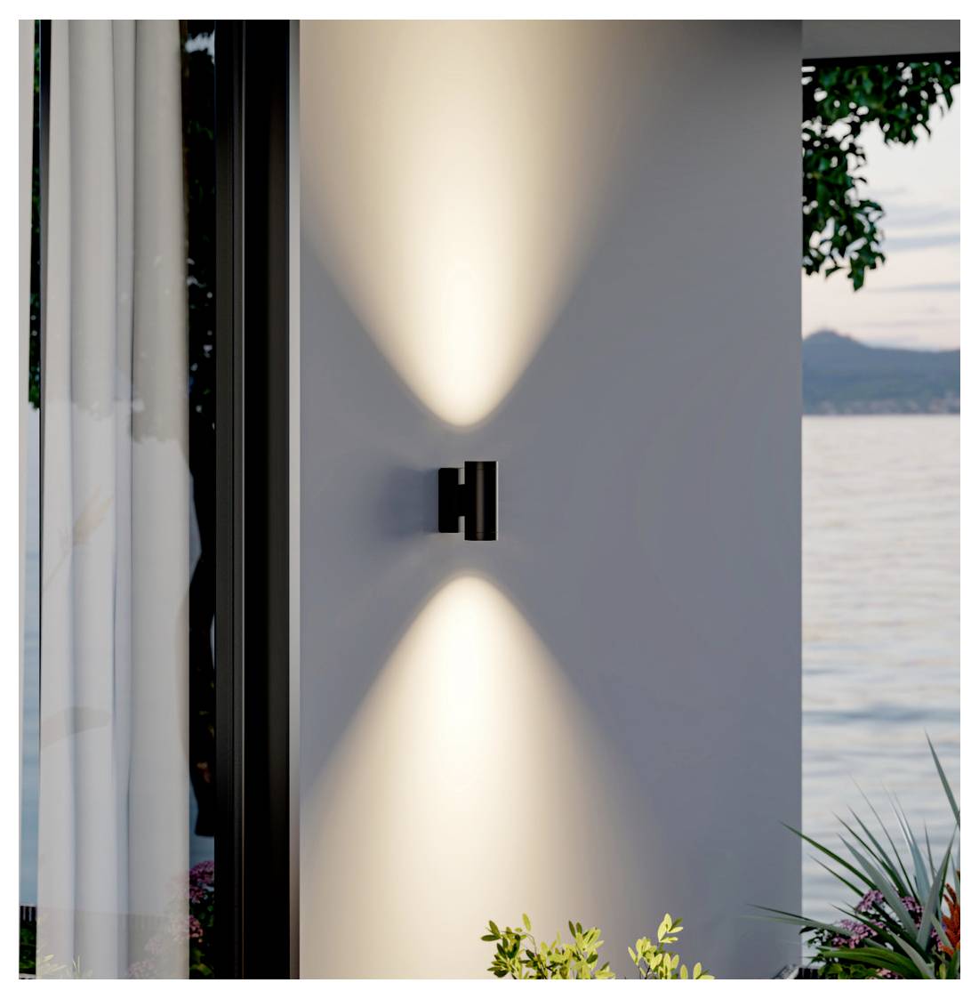 Moderne Wandleuchte, die symmetrische warme Lichtstrahlen auf eine weiße Außenwand neben einem Fenster wirft, mit Seeblick und Pflanzen in der Nähe.