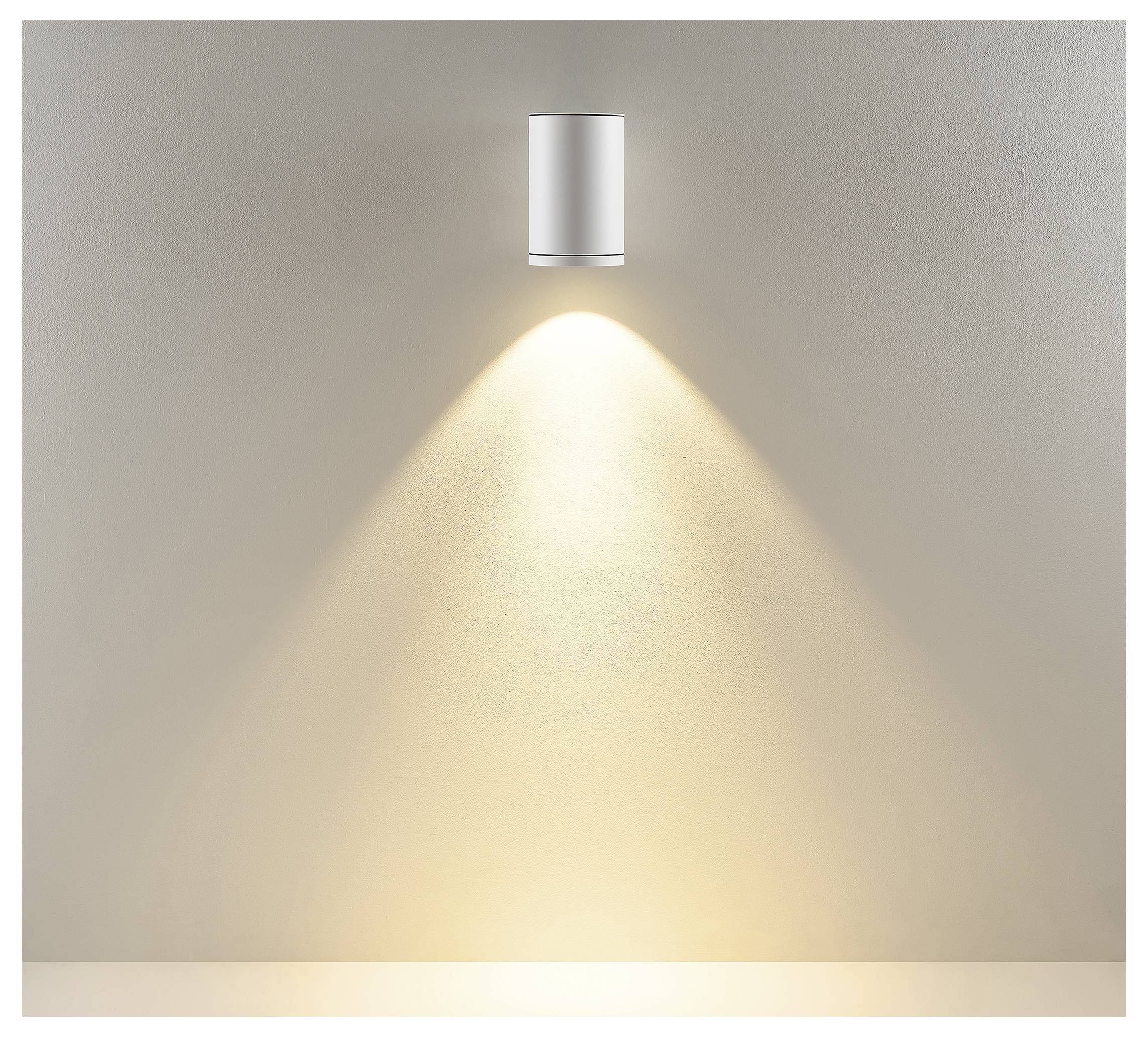 An der Wand montierte zylindrische Leuchte, die einen warmen, nach unten gerichteten Lichtkegel auf eine schlichte Wand wirft.