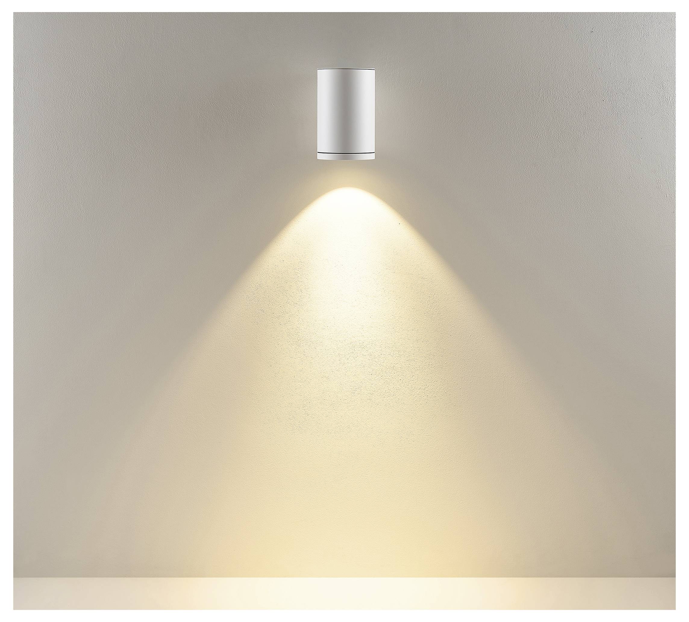 An der Wand montierte zylindrische Leuchte wirft einen warmen Lichtkegel nach unten auf eine schlichte beigefarbene Wand.