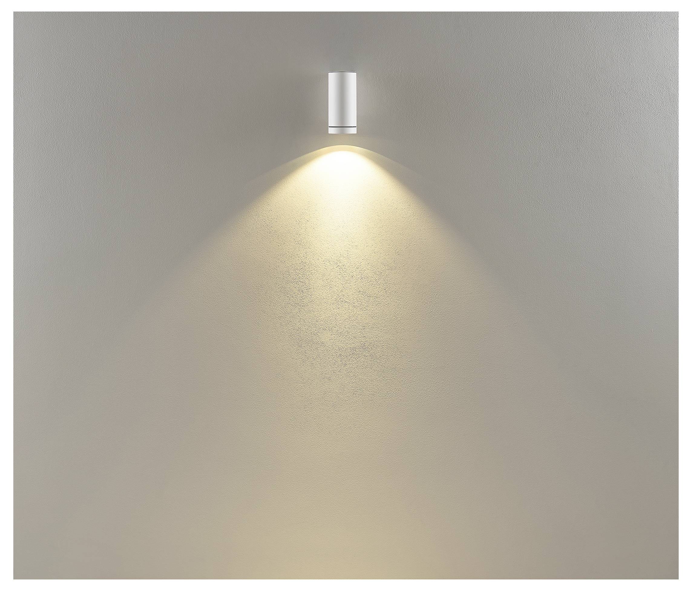 An der Wand montierte silberne Leuchte, die einen warmen Lichtkegel auf eine schlichte beigefarbene Wand wirft.