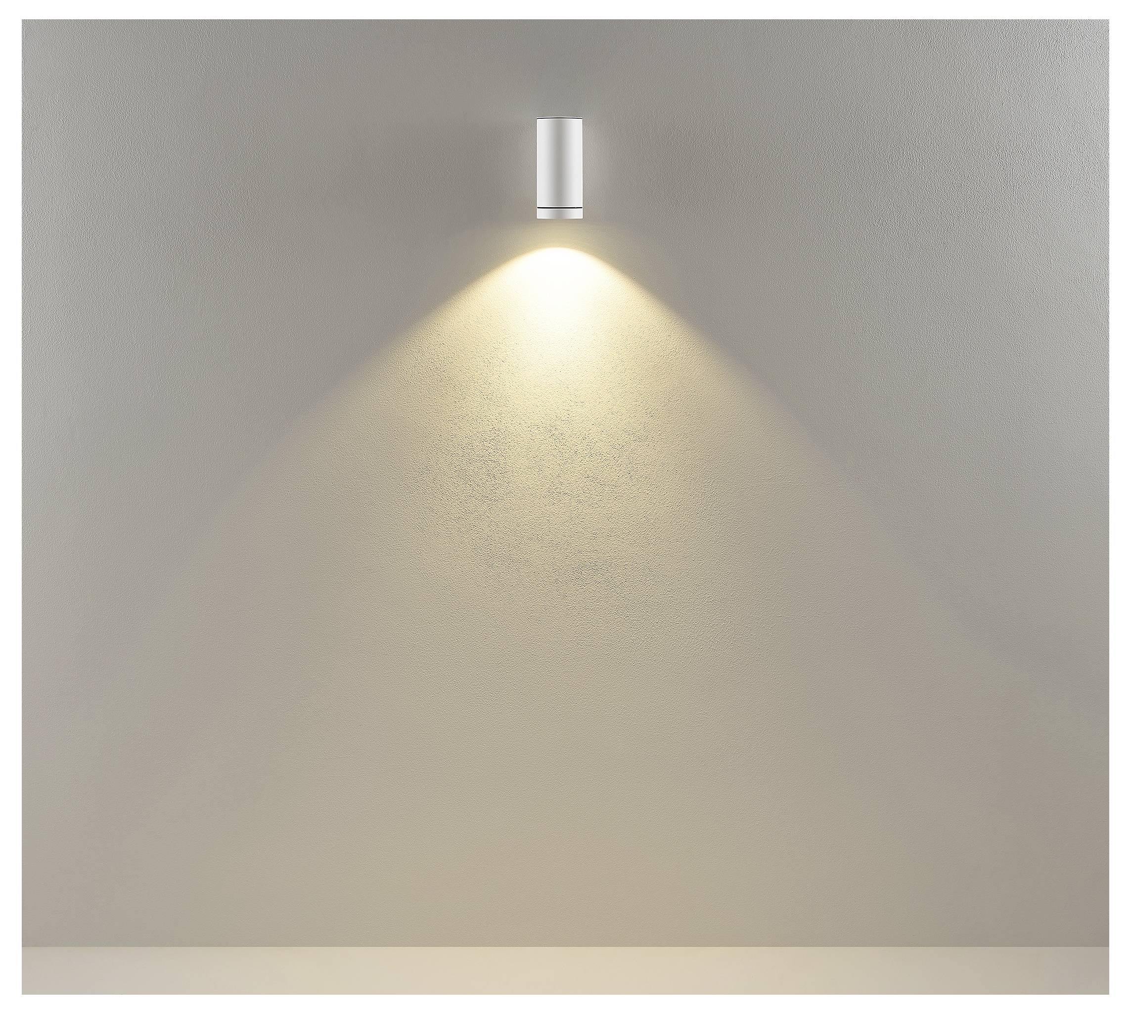 An der Wand montierte zylindrische Leuchte, die einen warmen Abwärtsstrahl auf eine schlichte beige Wand wirft.